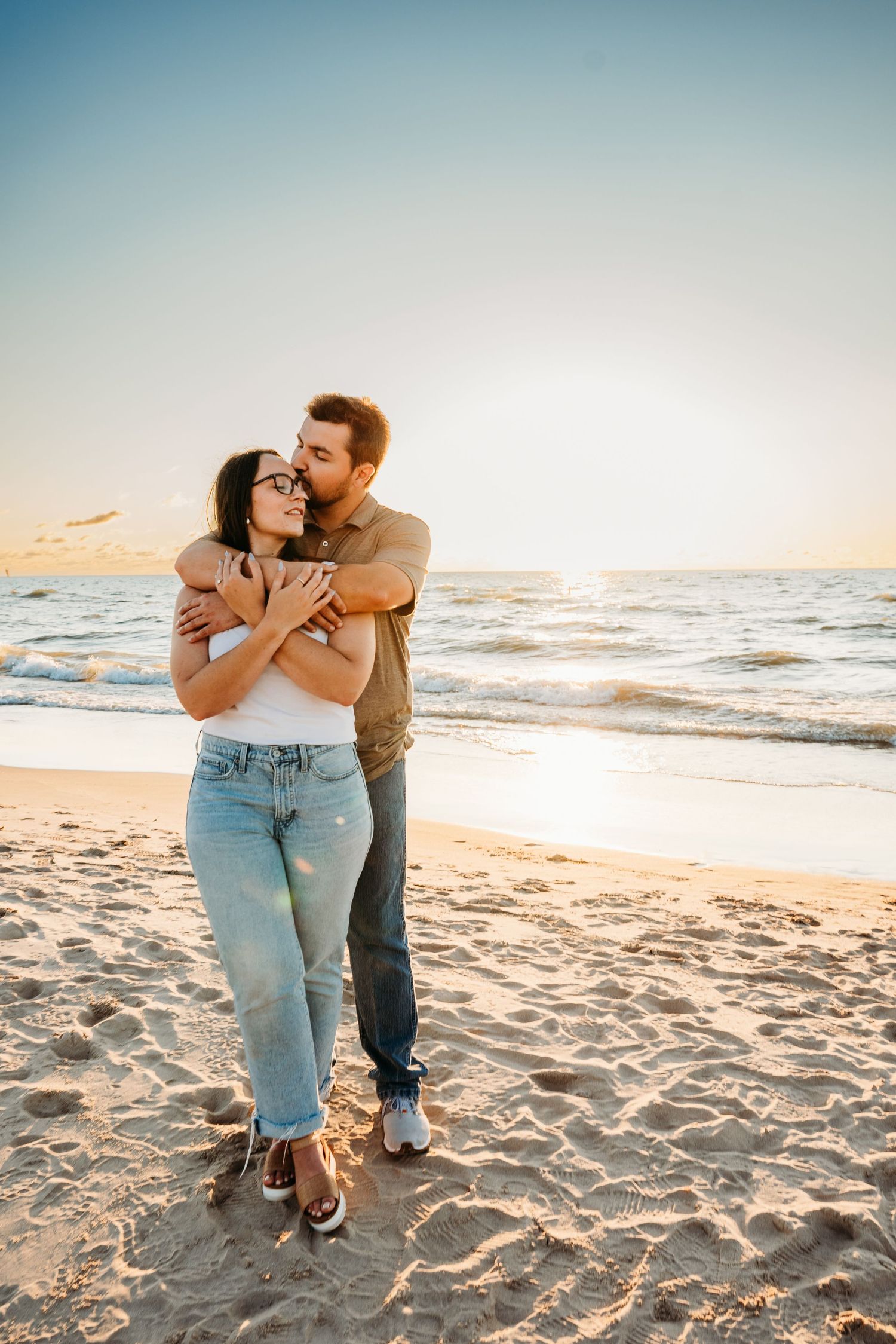 A couple shares a tender moment together while sitting on a sandy beach at sunset.