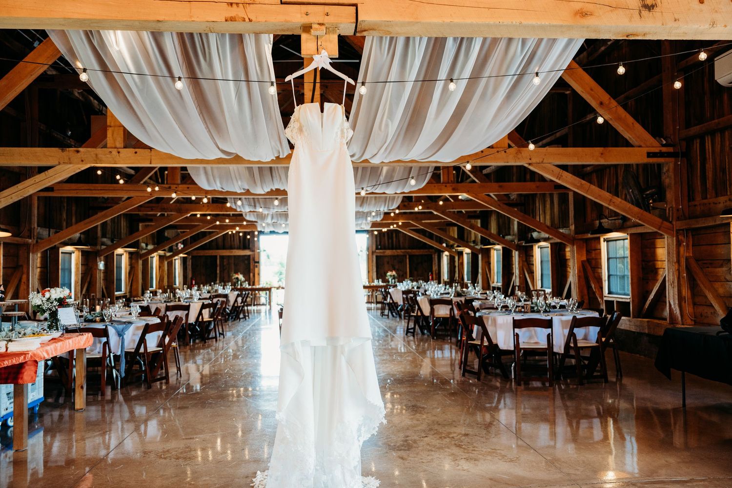 A rustic wooden barn venue decorated with string lights and white fabric draping for an elegant wedding reception.