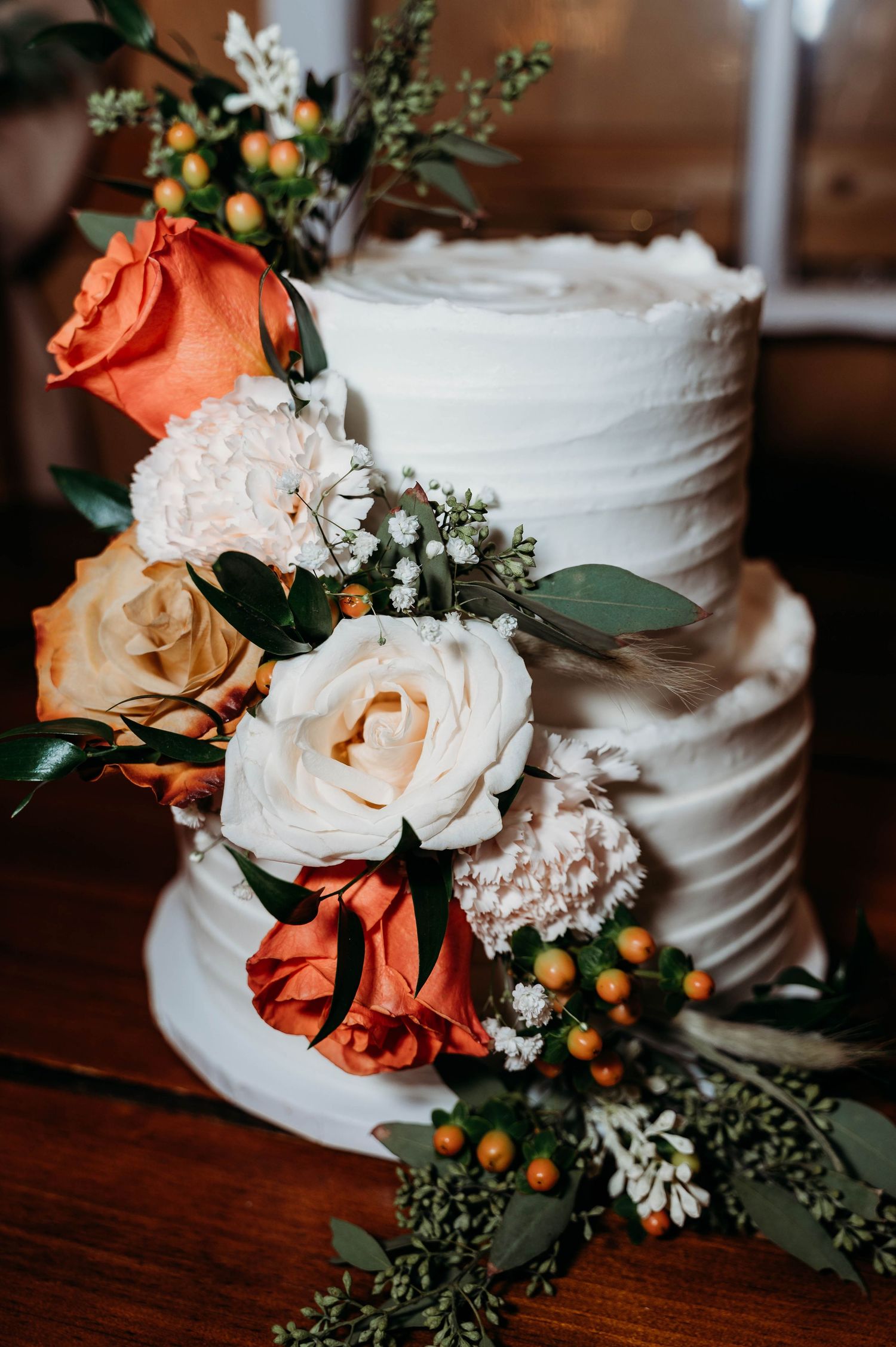 Close-up details of a white wedding cake decorated with peach and coral roses, greenery, and small orange berries.