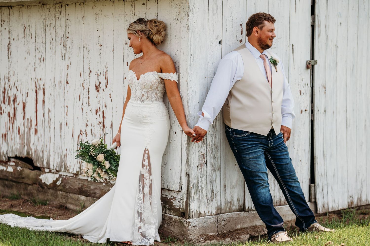 A rustic white barn wall serves as a backdrop for a romantic wedding photo shoot.