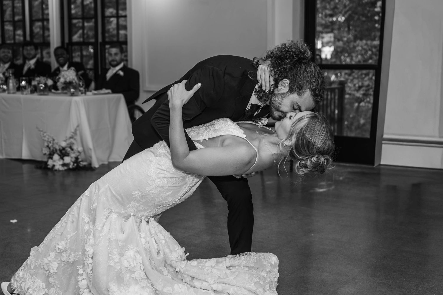 Black and white photo of bride and groom sharing a romantic dip kiss during their first dance at wedding reception.