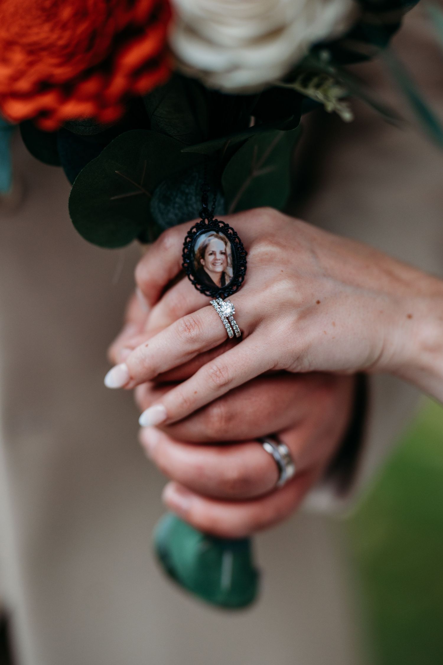 Close-up of hands holding a bridal bouquet with red flowers, showcasing an elegant engagement ring.