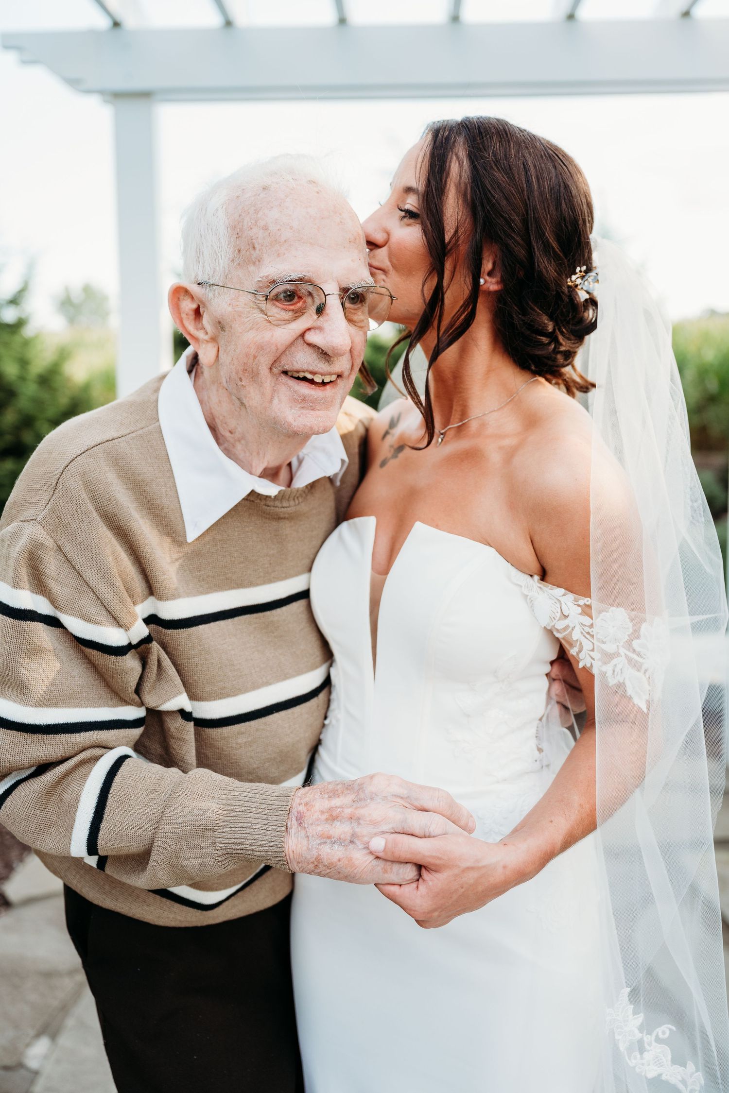 A tender moment captured between a bride in white and an elderly guest in a tan suit during a wedding celebration.