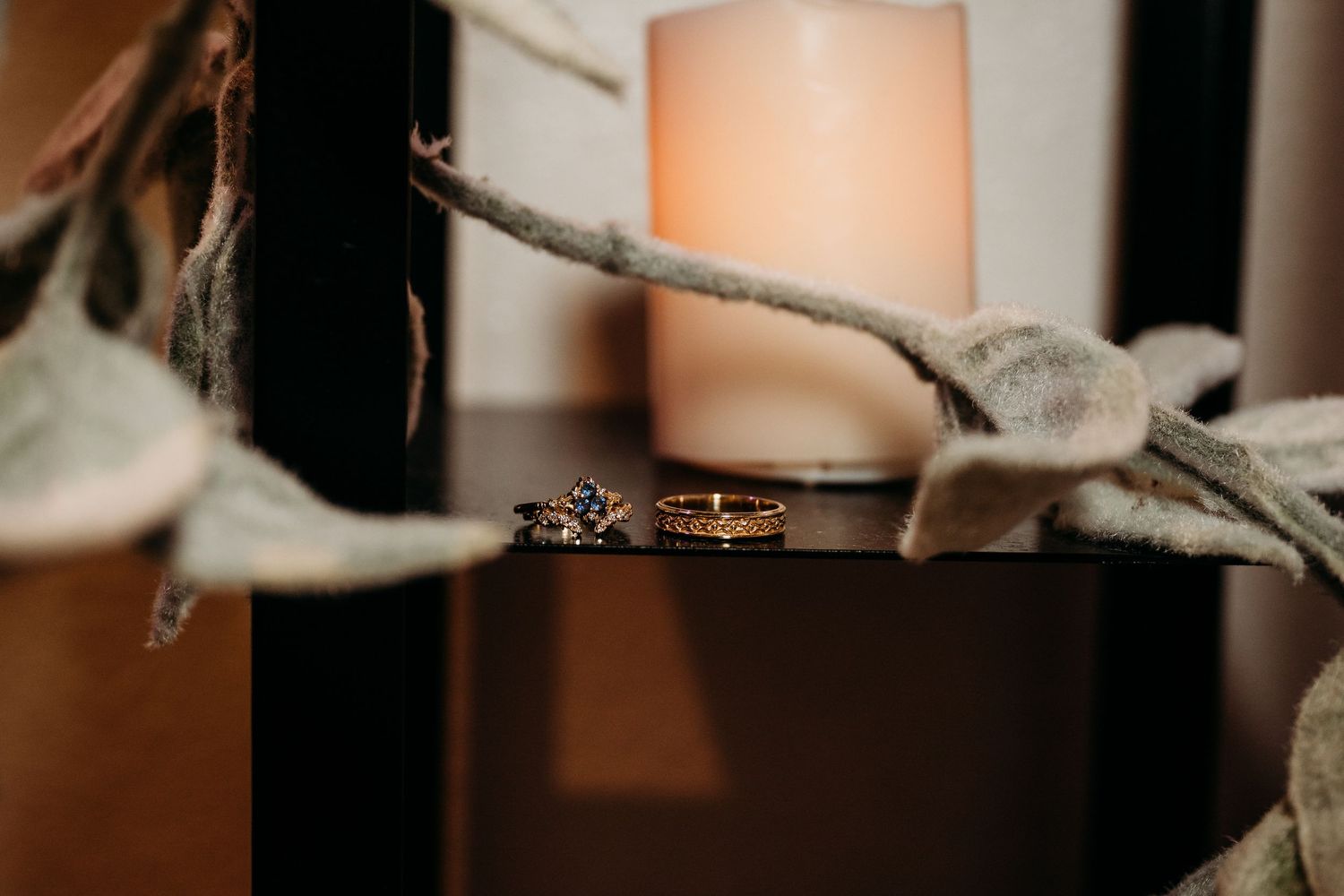 Wedding rings displayed on a branch with a soft glowing candle in the background creating romantic ambiance.