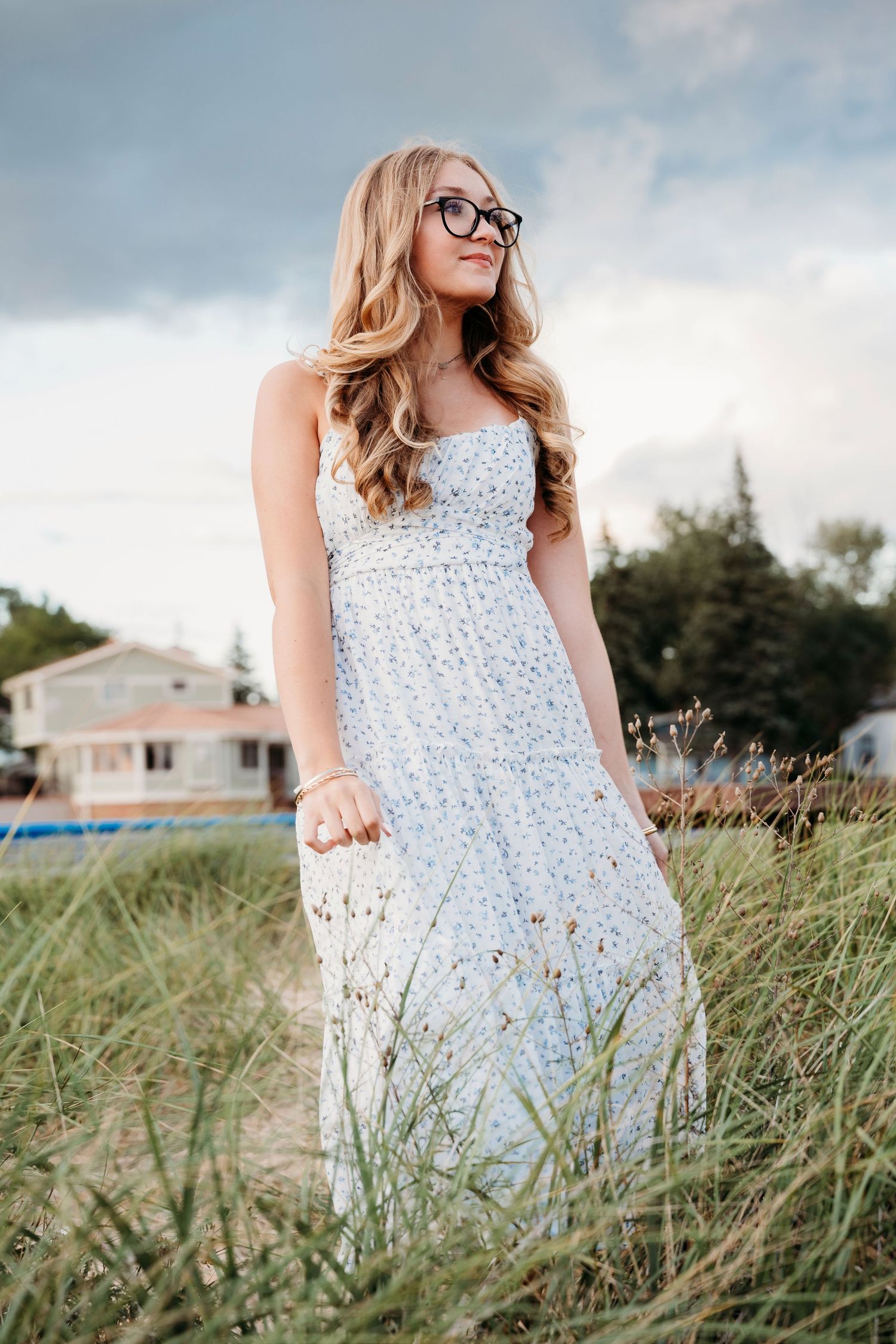 Multiple frames of someone wearing a white floral sundress standing in tall beach grass with houses visible in background.
