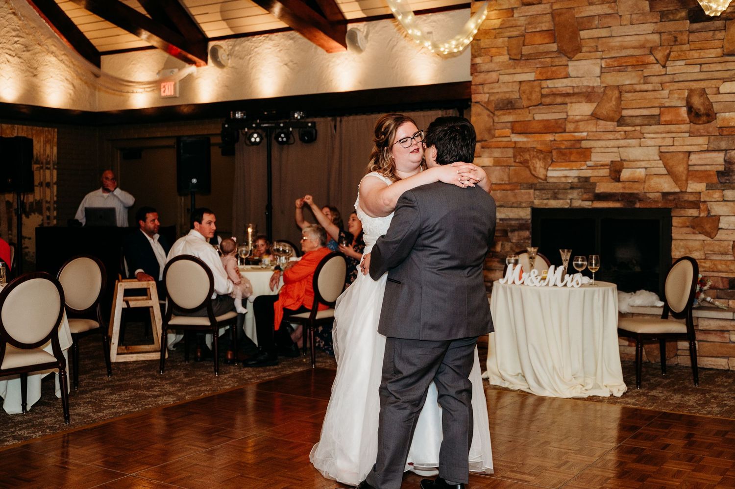 A couple shares their first dance at a rustic indoor wedding reception with stone walls and elegant table settings. Kalamazoo Wedding