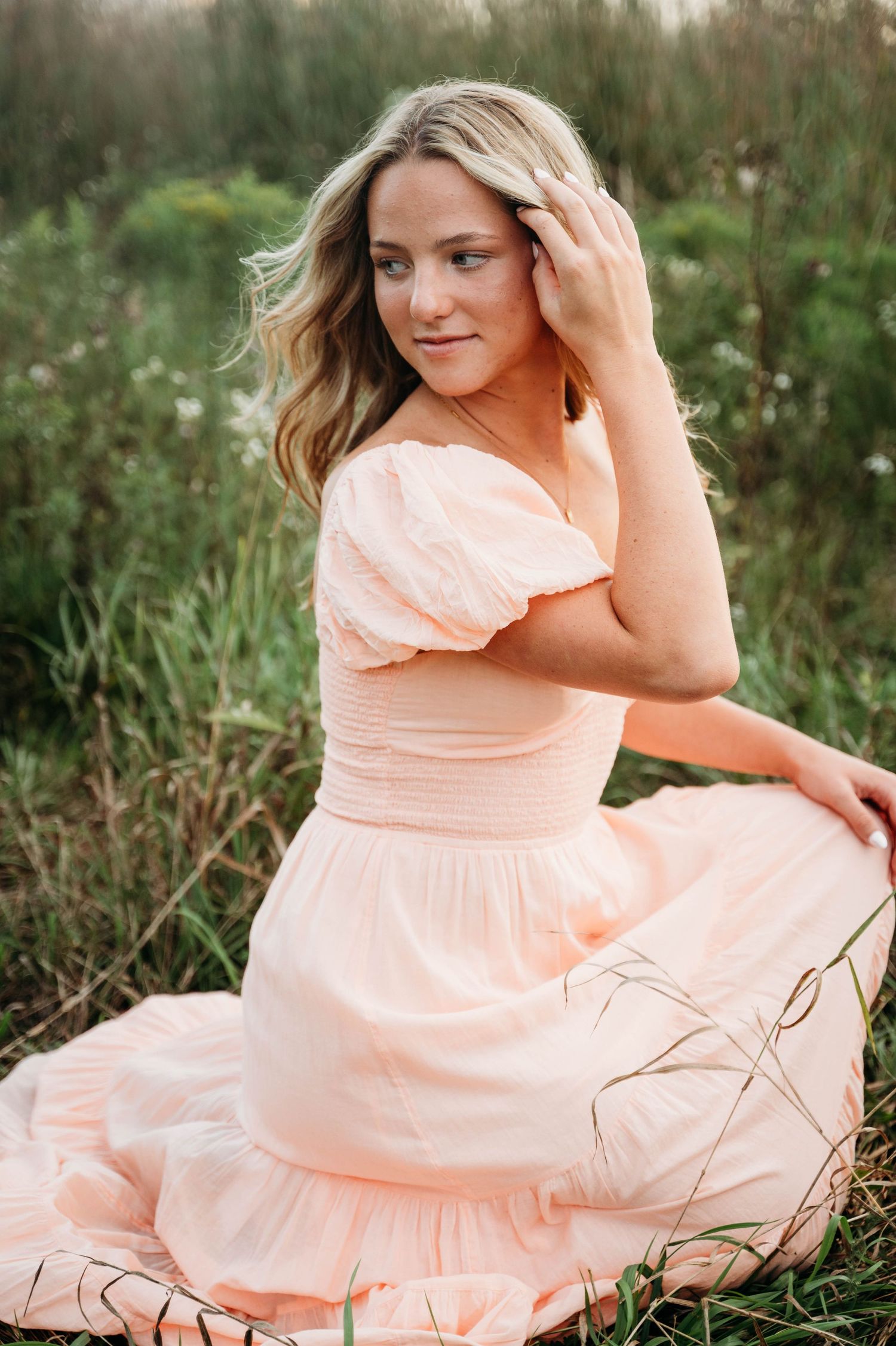 Beautiful portrait in peach dress sitting in wildflower field during golden hour photography session.