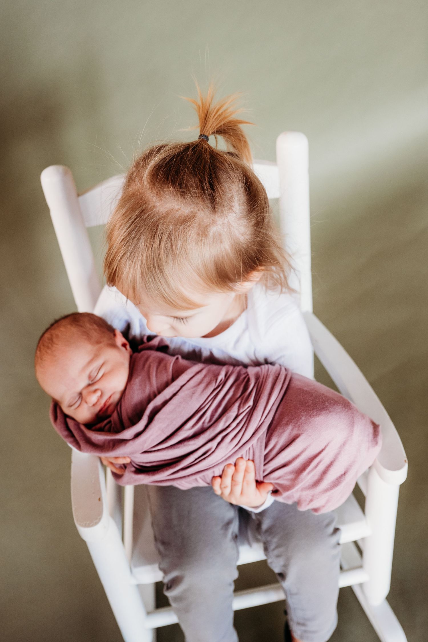 A sleeping baby in a white rocking chair wears a pink sweater and gray pants while napping in different positions.