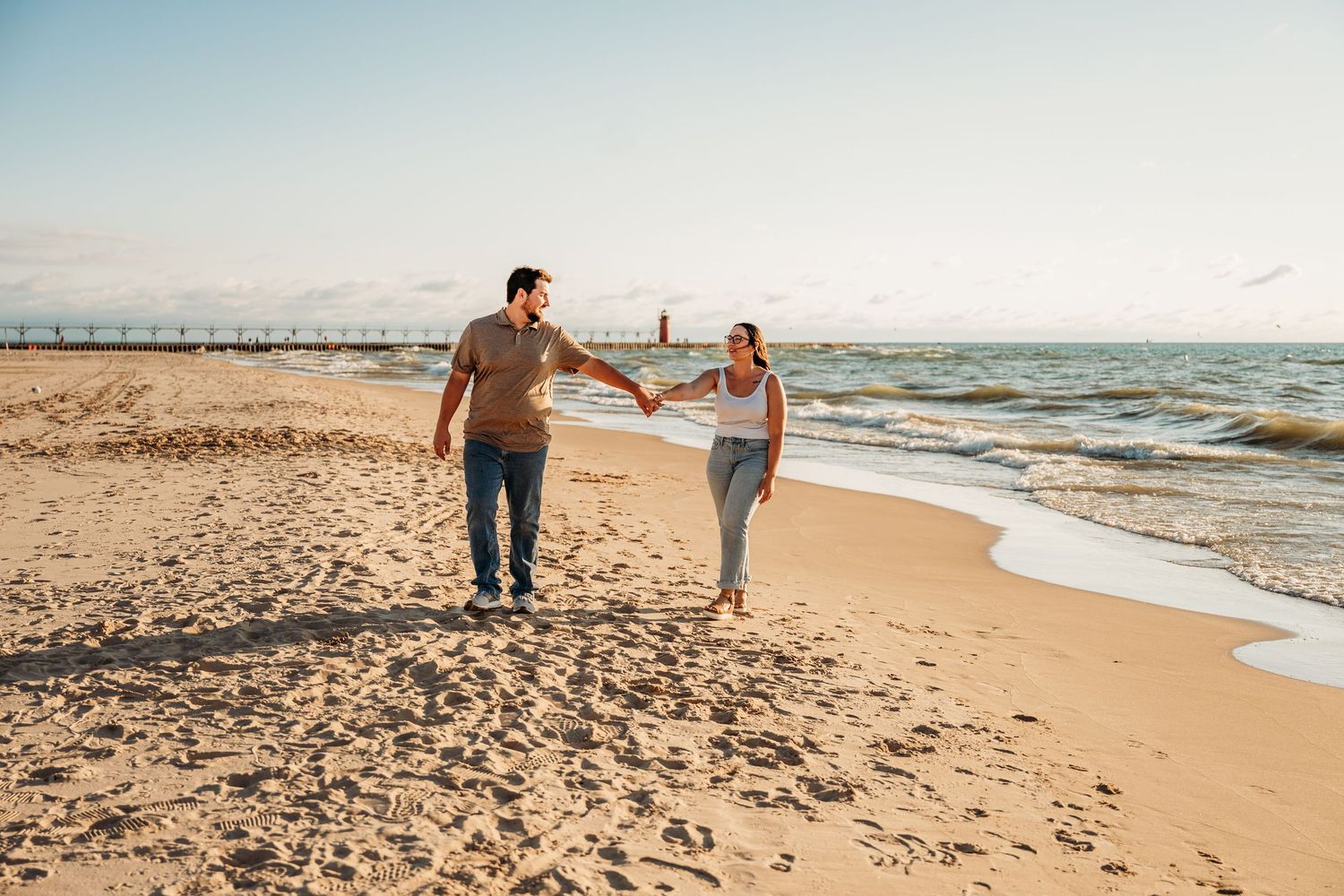 Couple walking hand in hand along a peaceful beach at sunset with waves gently rolling onto shore.