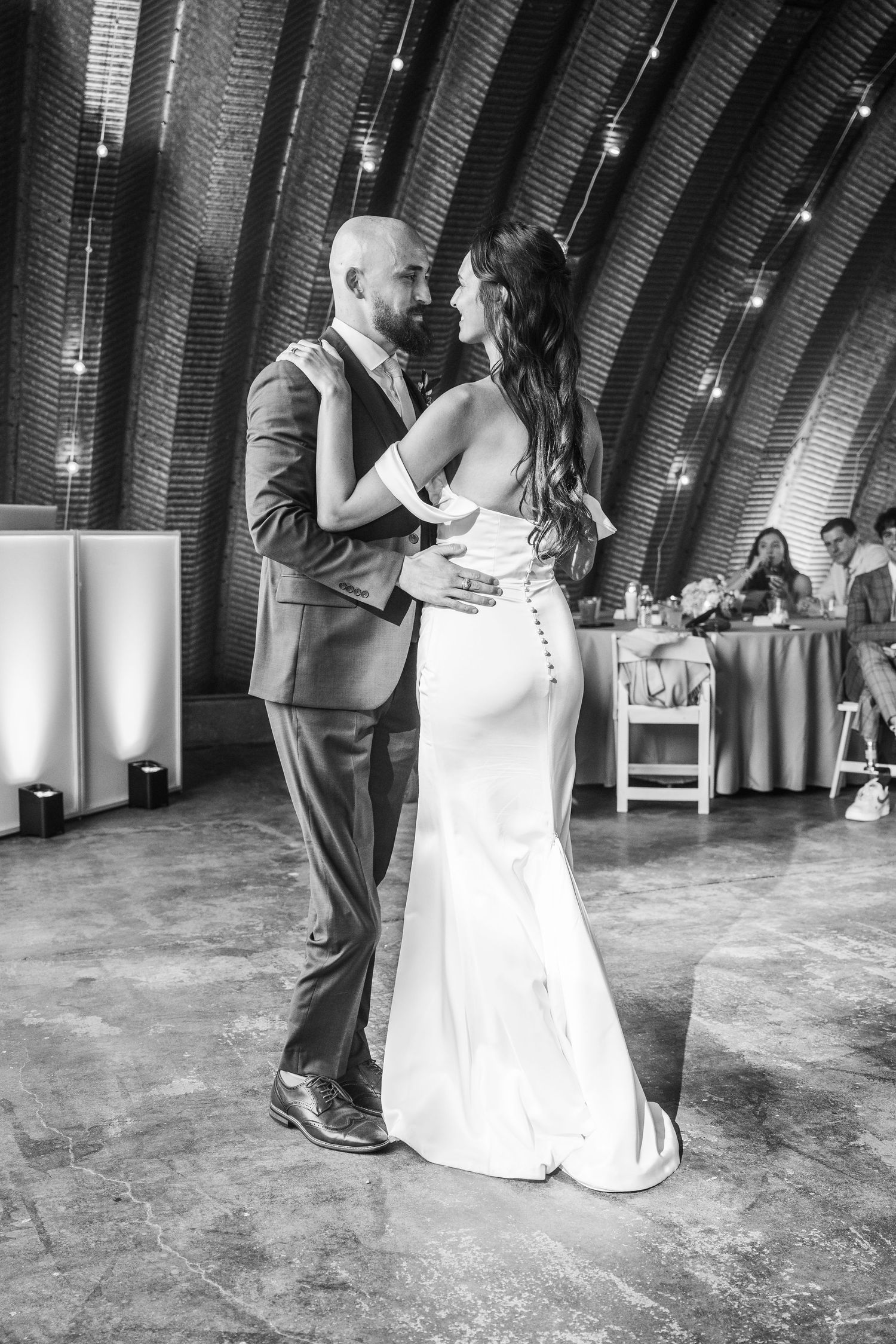 Bride and groom share their first dance in a rustic arched venue with string lights in black and white photo.