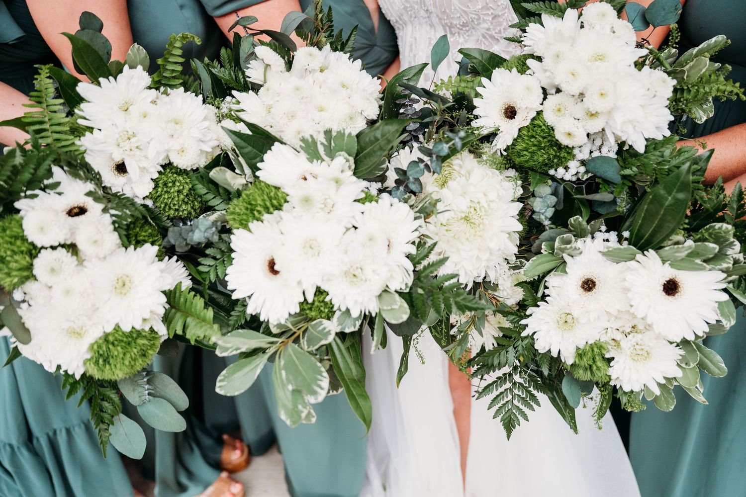 Bridesmaids in teal dresses holding lush white dahlia and greenery wedding bouquets.