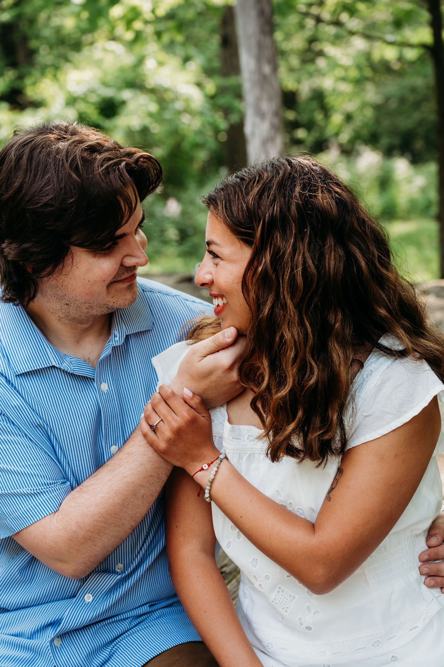 An intimate moment shared between a couple gazing at each other outdoors with natural greenery in the background.