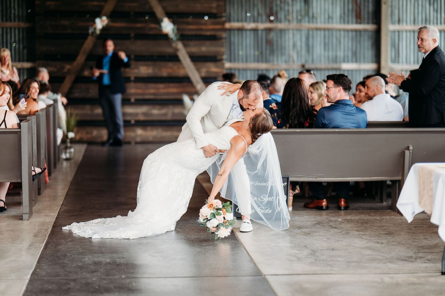 Wedding reception dance scene in rustic barn venue with string lights and wooden benches.