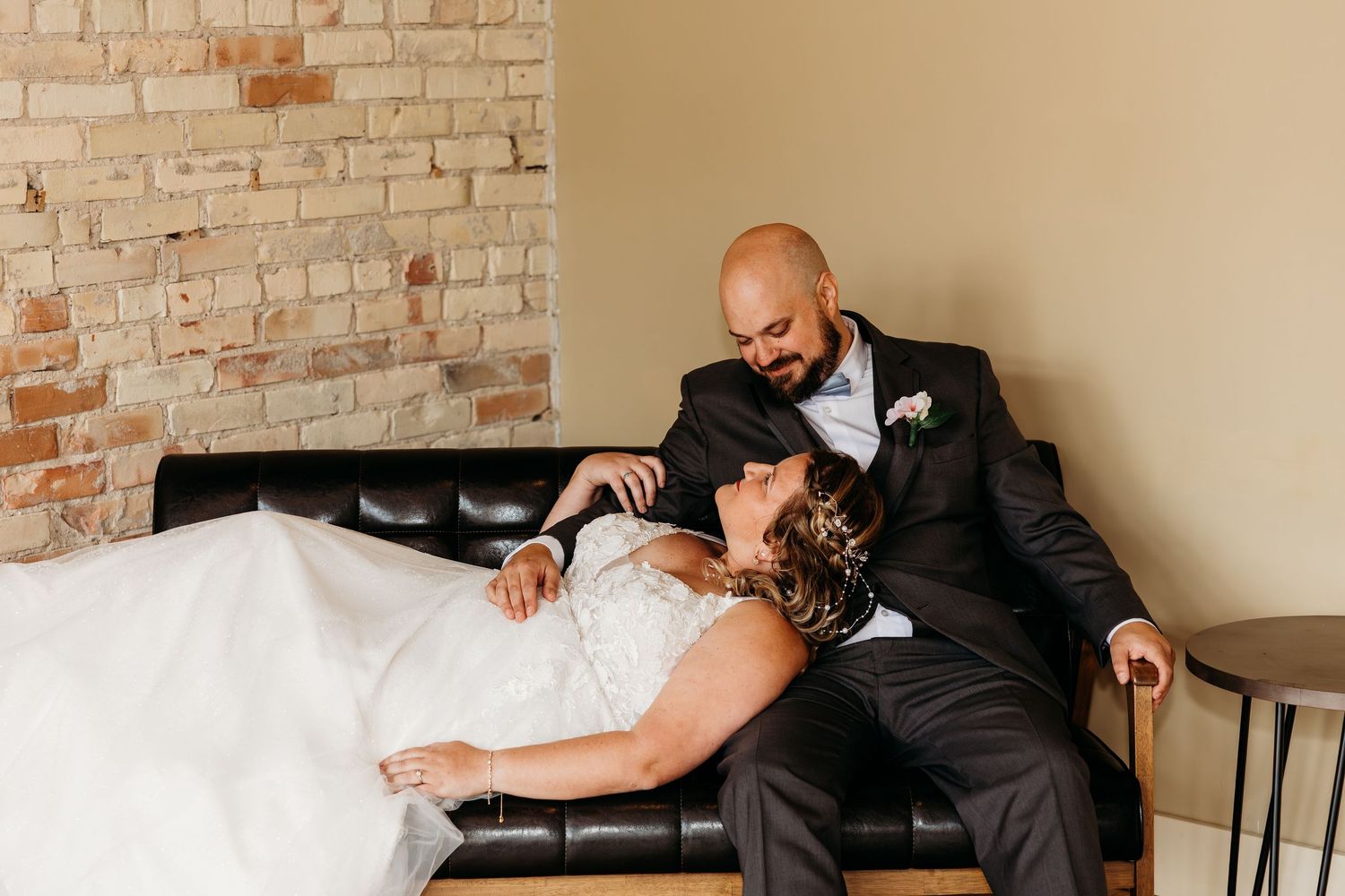 A person in a dark suit lays slumped over in a chair against a brick wall.