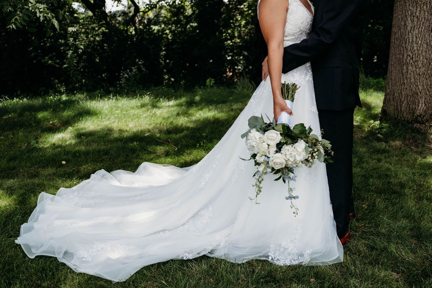 A dramatic wedding dress train flows across green grass with cascading white flowers.