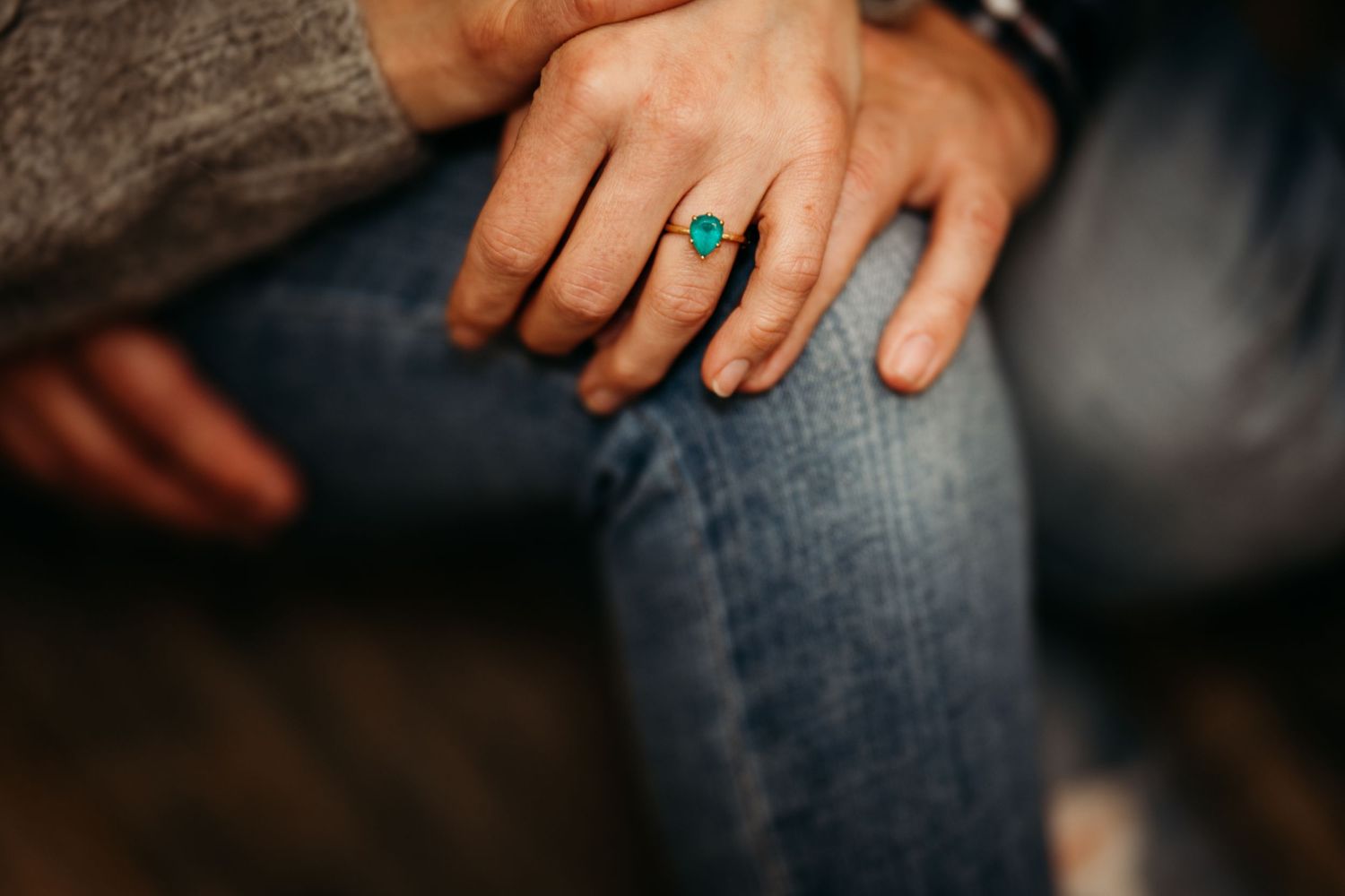 Hand wearing a turquoise ring rests on denim jeans in a warm atmospheric lighting setting.