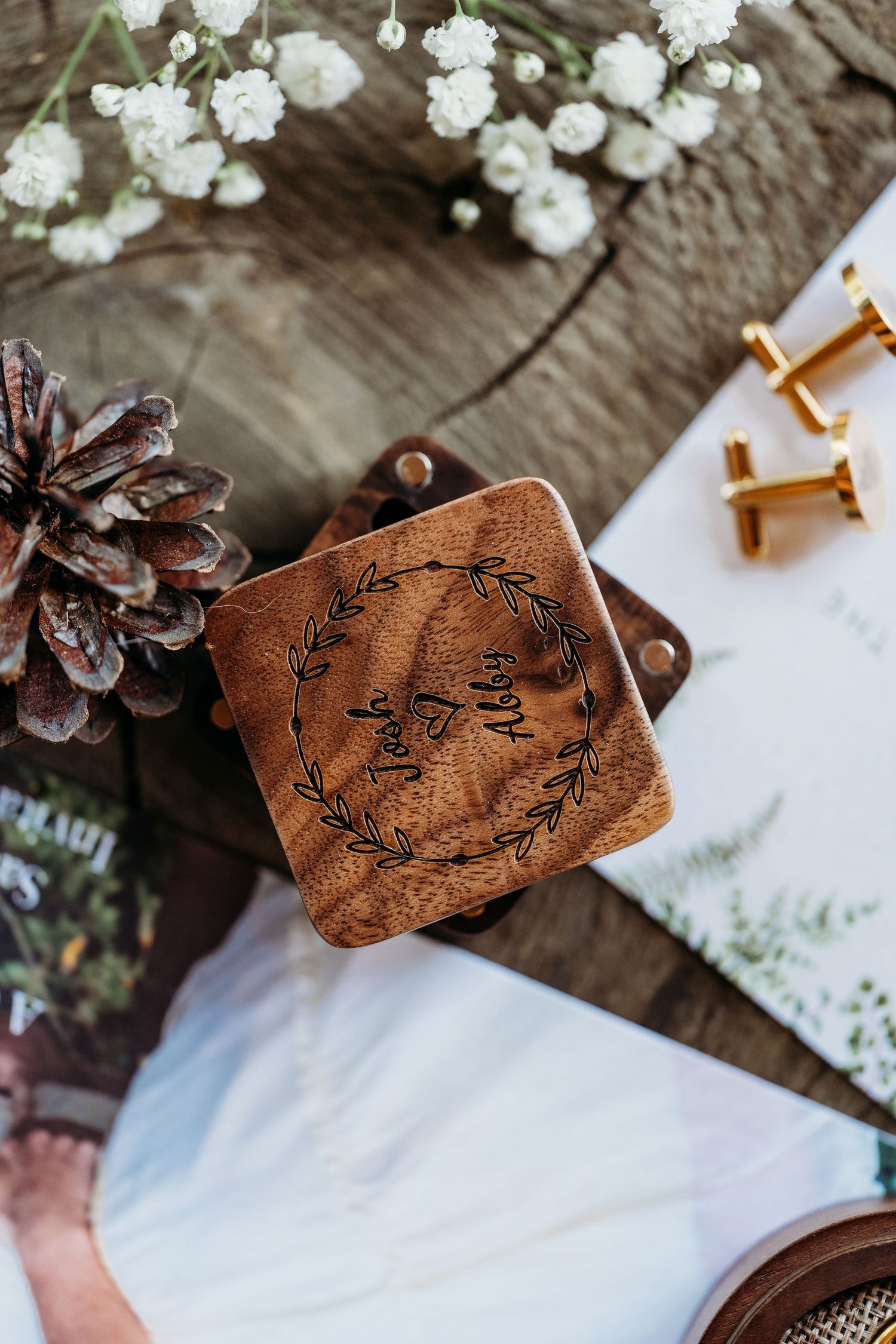 Wooden wedding place cards with floral designs arranged with pinecones and white flowers on a rustic surface.