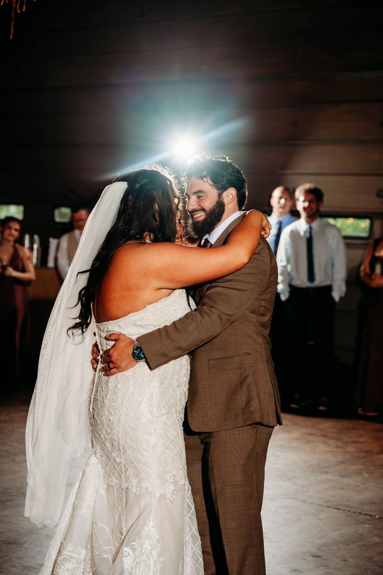 Bride and groom share their first dance, smiling and embracing in a warmly lit wedding reception venue.