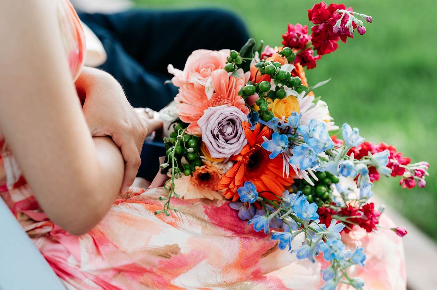 Bride holding a vibrant wedding bouquet with pink roses, red, blue, and orange flowers in a colorful floral dress.