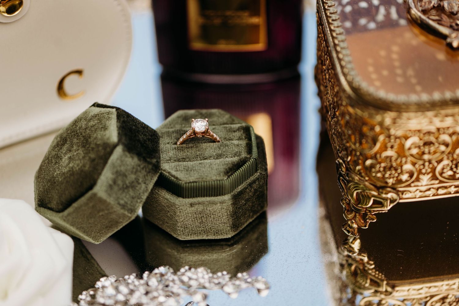 Vintage velvet ring box sits beside a gold ornate frame on a white surface with jewelry and decor in the background.