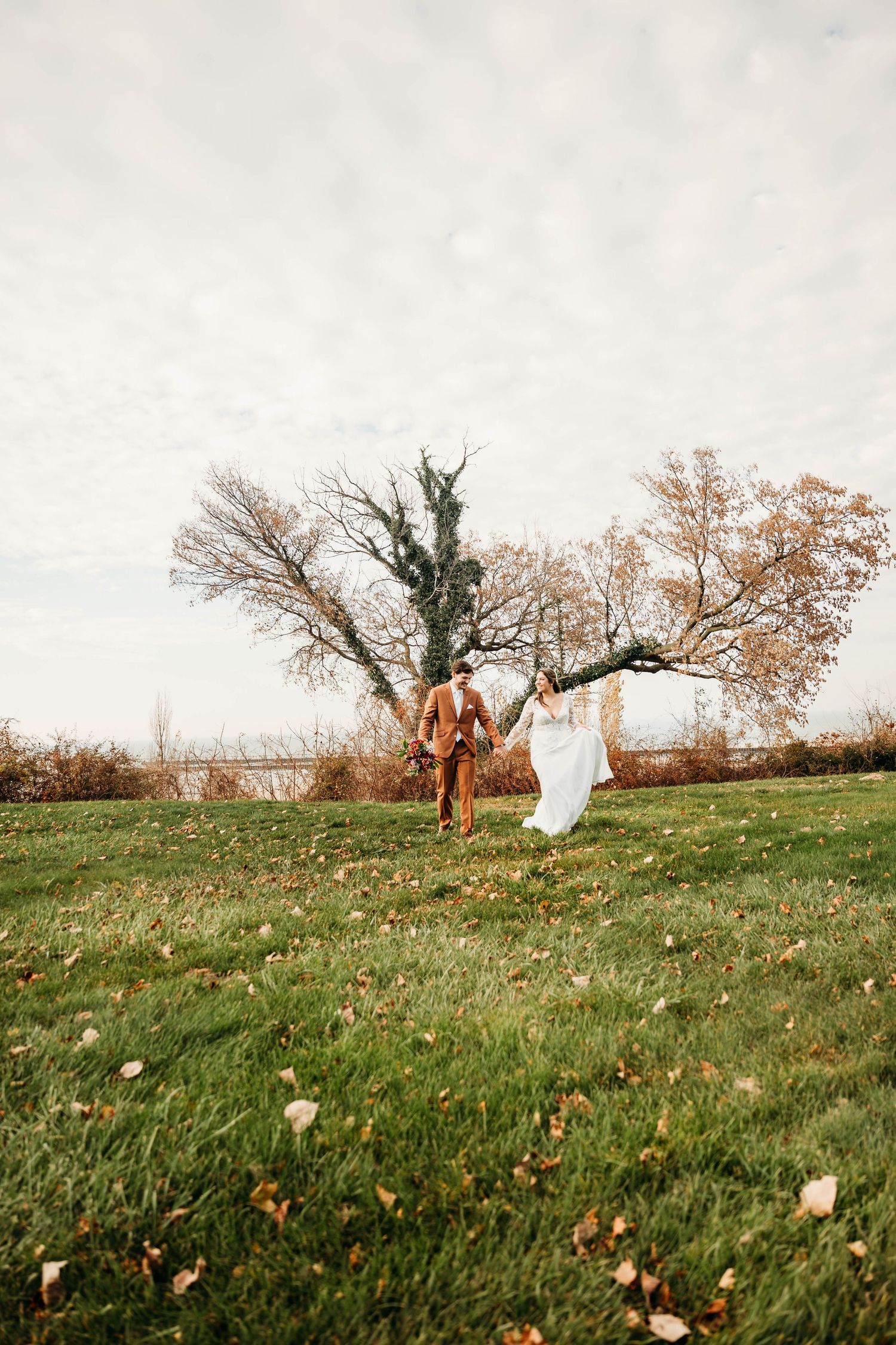 A person wearing brown clothing runs through an autumn field with white fabric flowing in the wind.