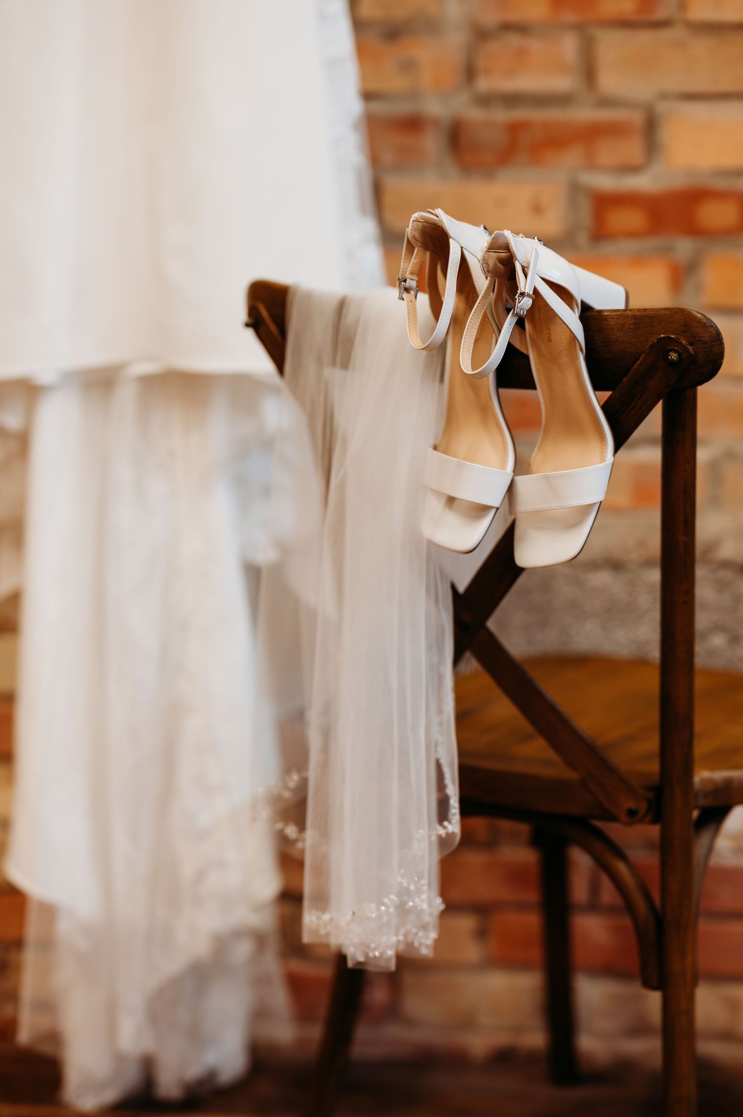 White wedding shoes and delicate lace veils displayed against a rustic brick wall backdrop.