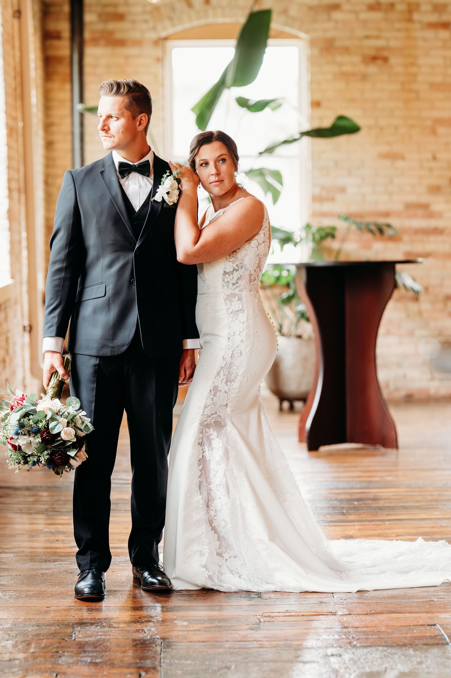 A couple in wedding attire walking together on a rustic brick floor in an elegant indoor venue.