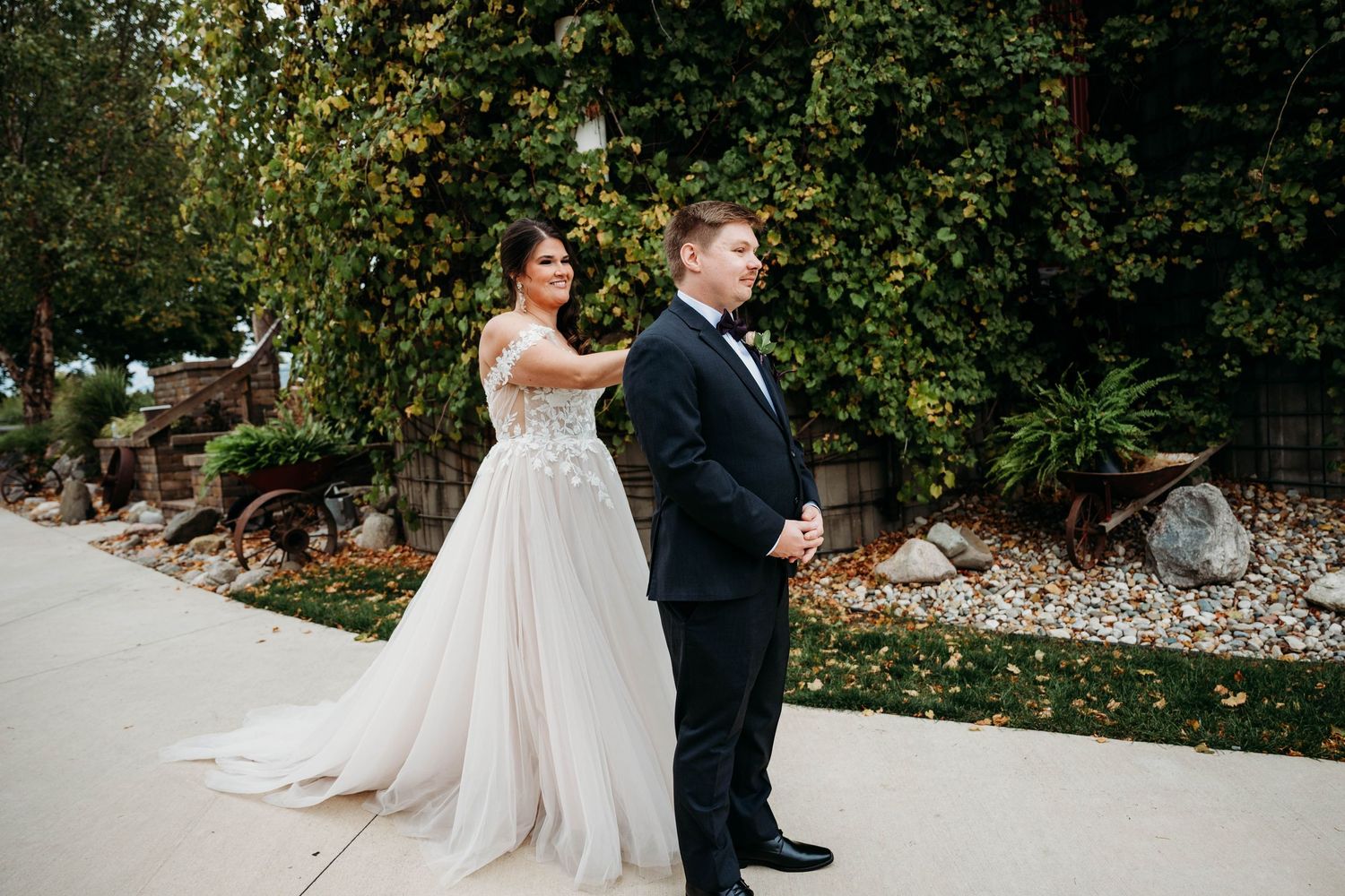 A couple in formal wedding attire stands together in a lush garden setting during their special day.