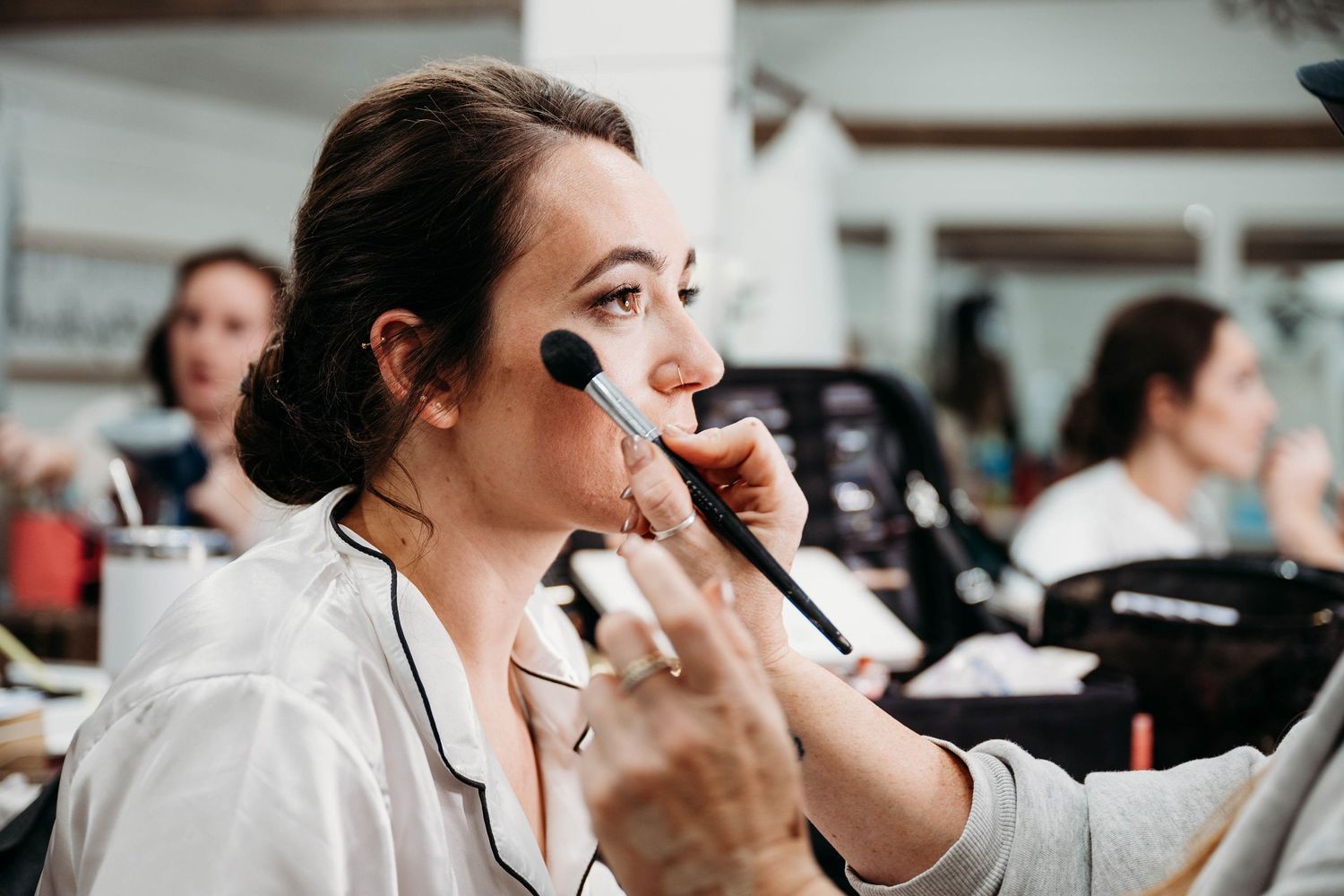 Makeup artist applying cosmetics with brushes in a professional beauty studio setting.