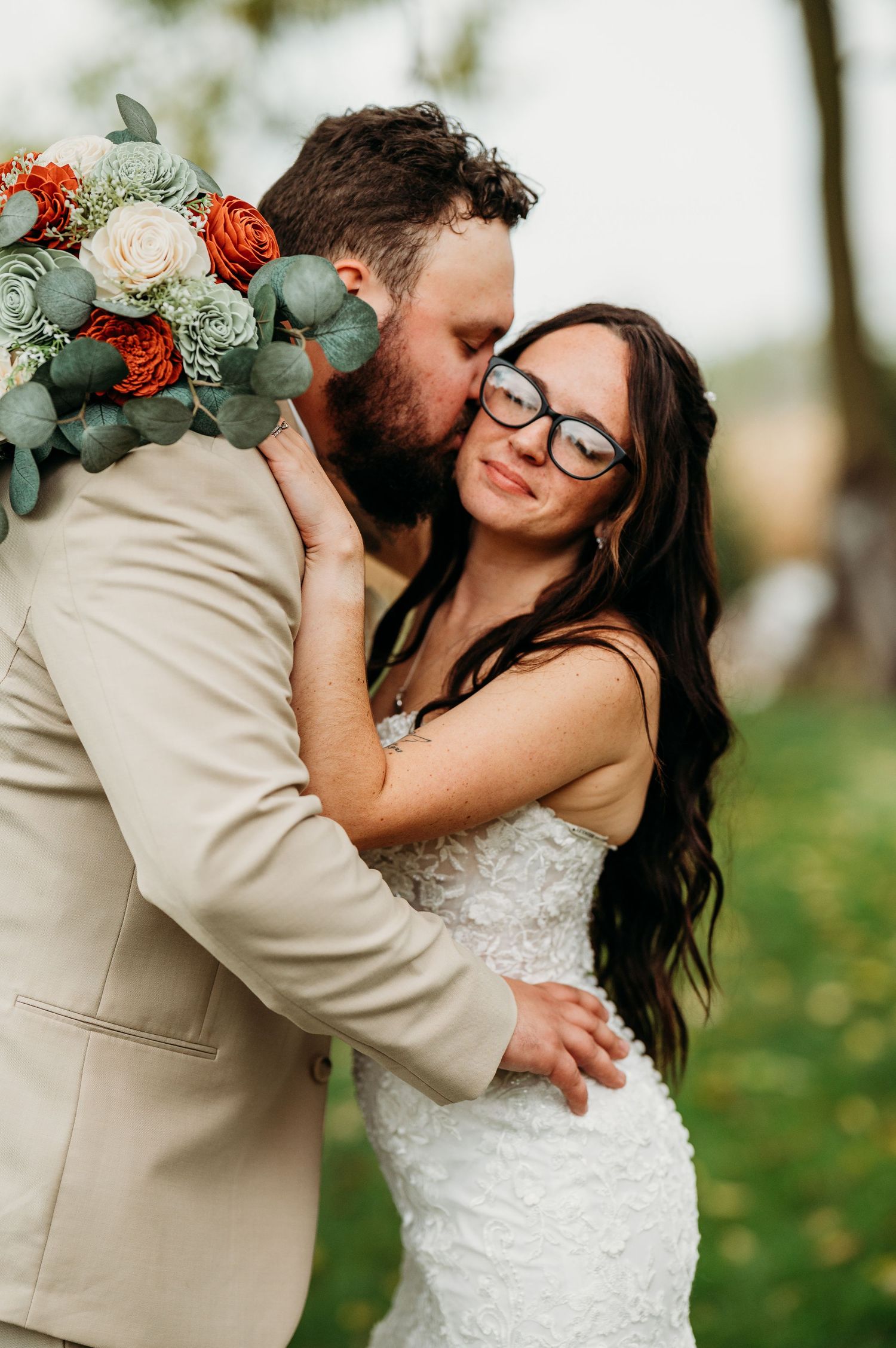 Newlyweds share intimate moment outdoors with bride holding coral and white bouquet with eucalyptus.
