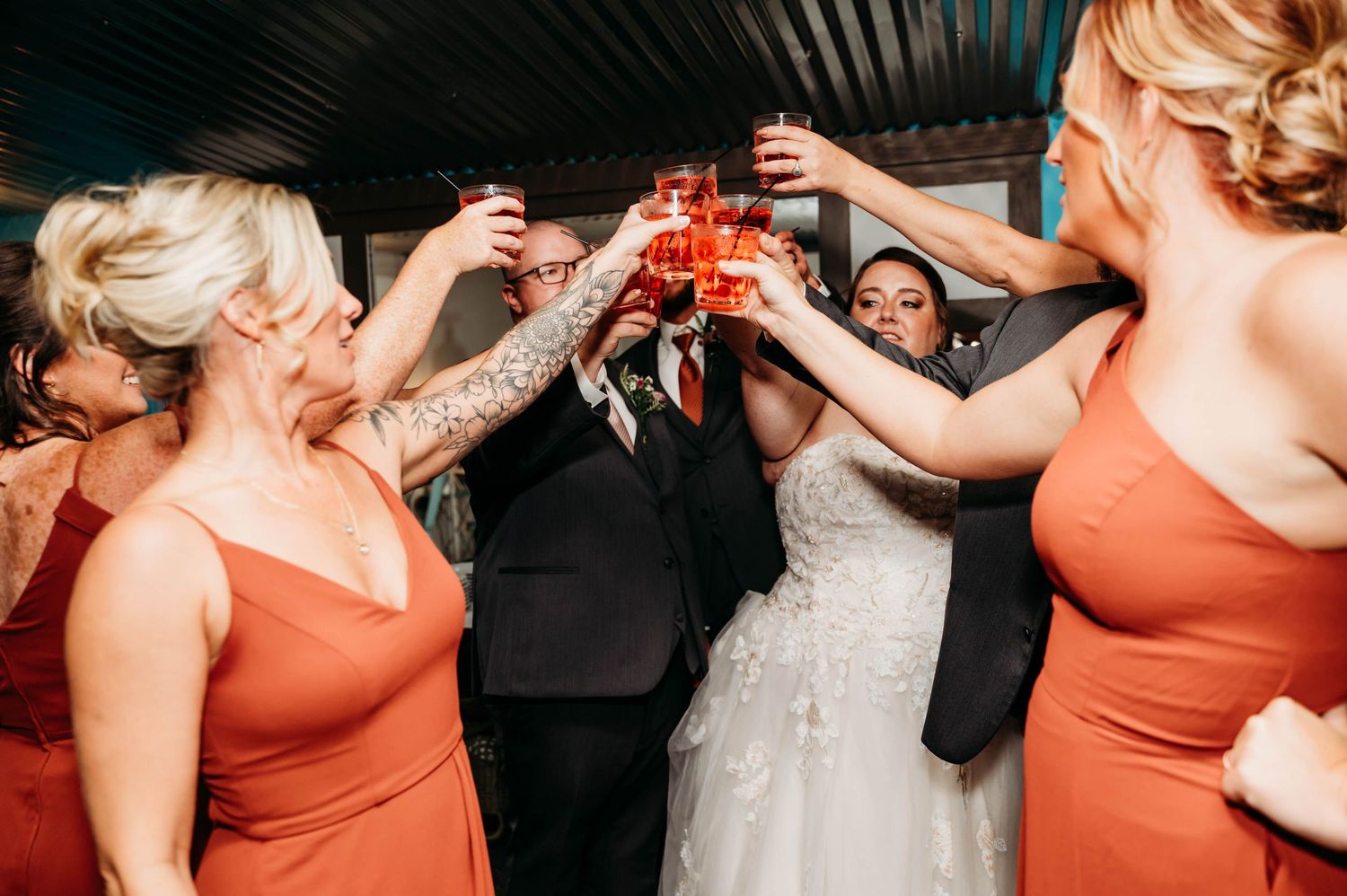 Wedding party in coral dresses toasting with drinks at a celebration.