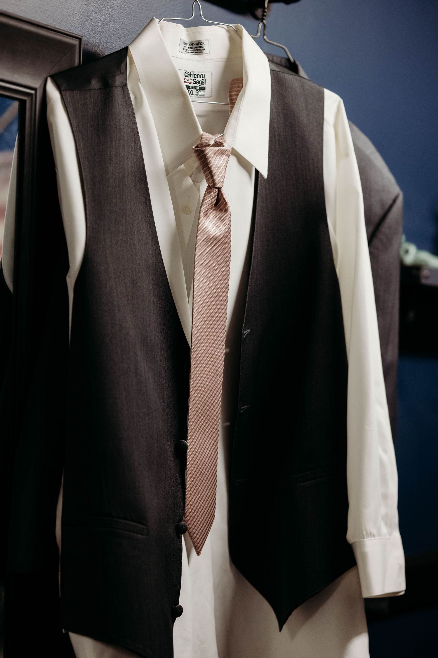 Row of formal black suits with white dress shirts and pink ties hanging on display.
