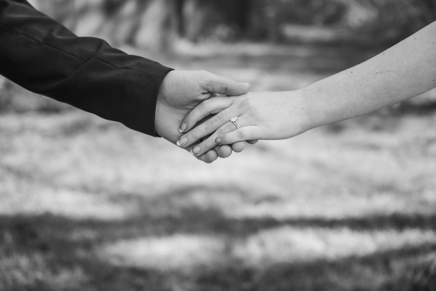 Black and white photo of a couple holding hands, with a diamond engagement ring visible on the woman's finger.