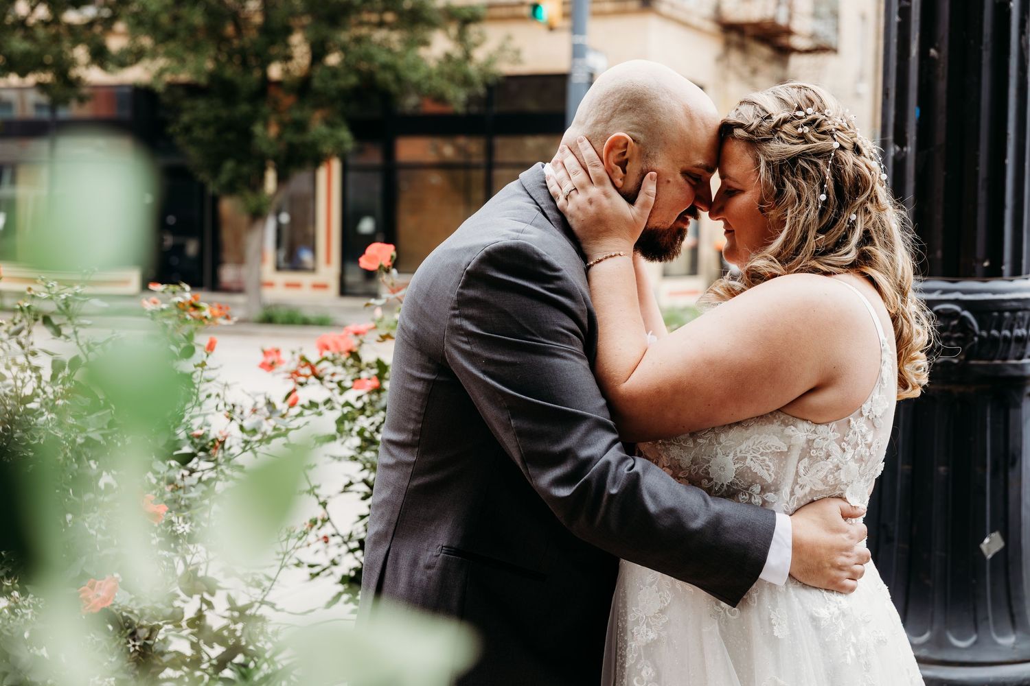 Bride and groom share a romantic forehead touch embrace outdoors, surrounded by blooming flowers on their wedding day.