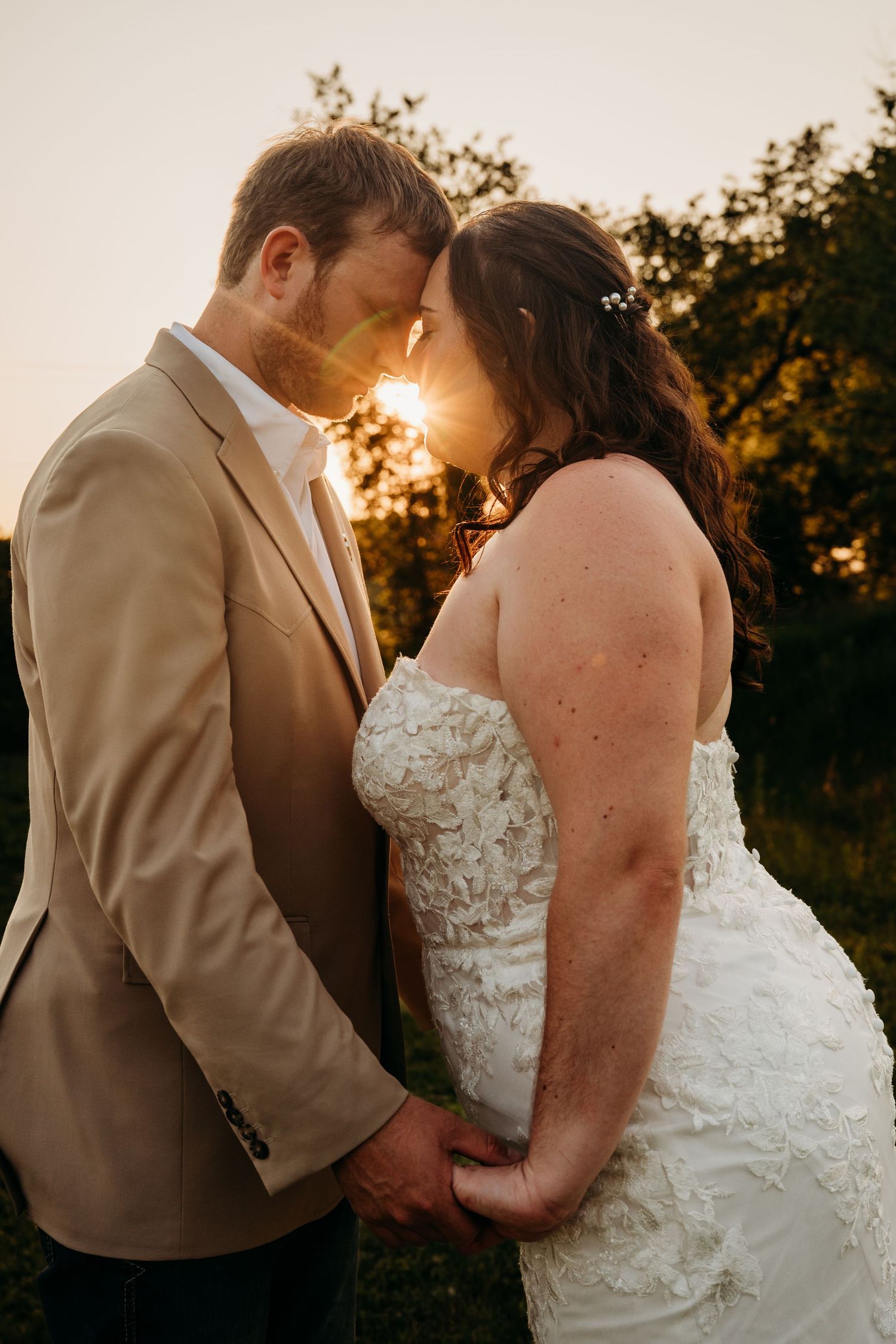 A romantic sunset wedding photograph with a couple embracing in warm golden light while wearing formal attire.
