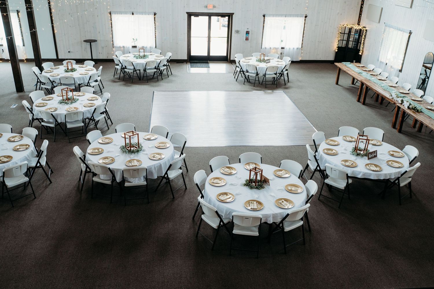 Multiple round white dining tables are set up in rows in an elegant banquet hall with minimalist decor.