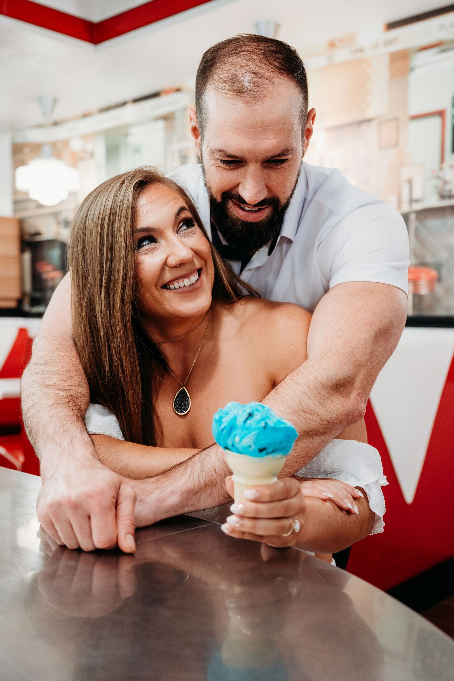 A joyful couple laughing while sharing a blue ice cream cone at a retro diner counter.