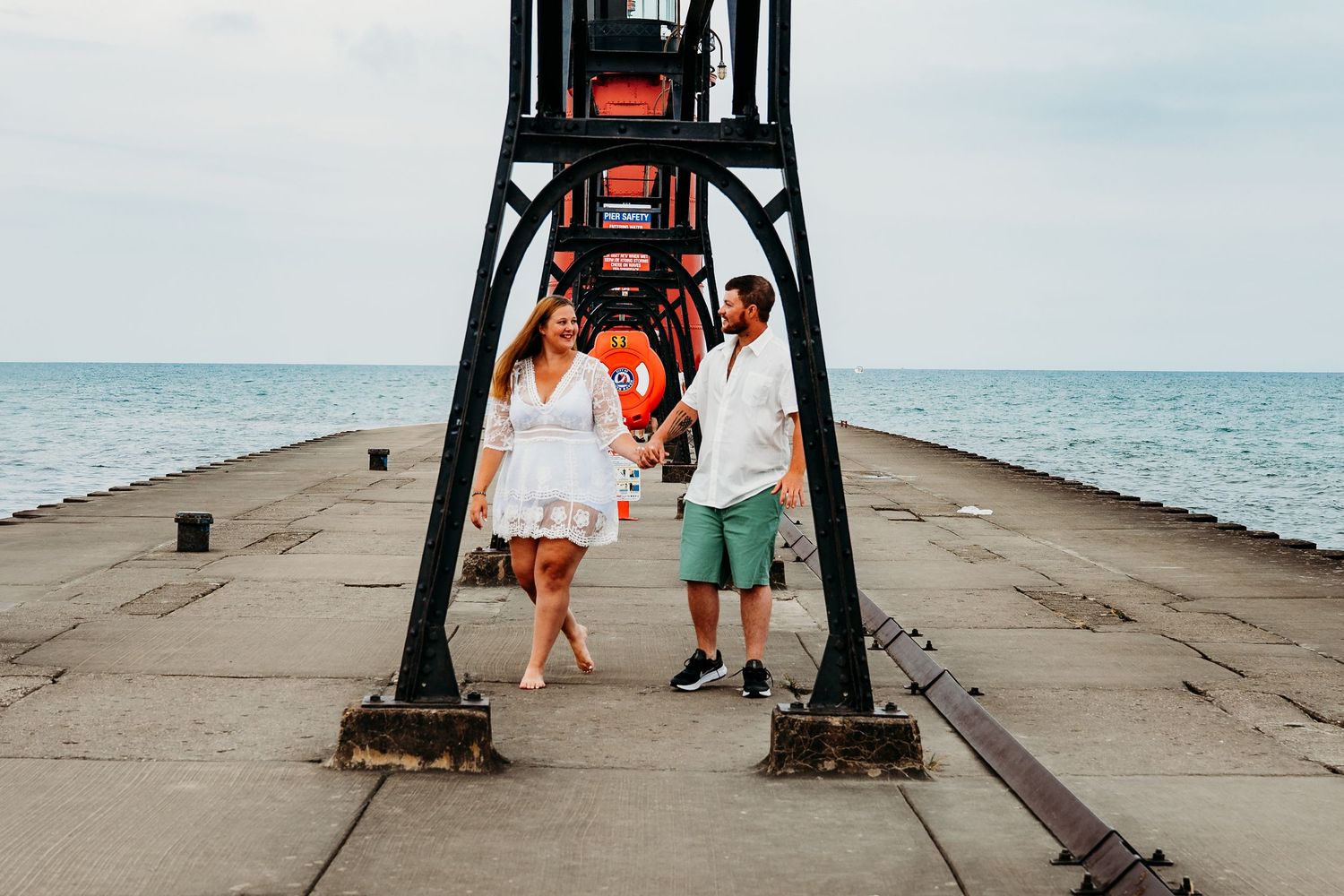A couple walking underneath a large metal structure at a beach pier creates a romantic silhouette against the sky.