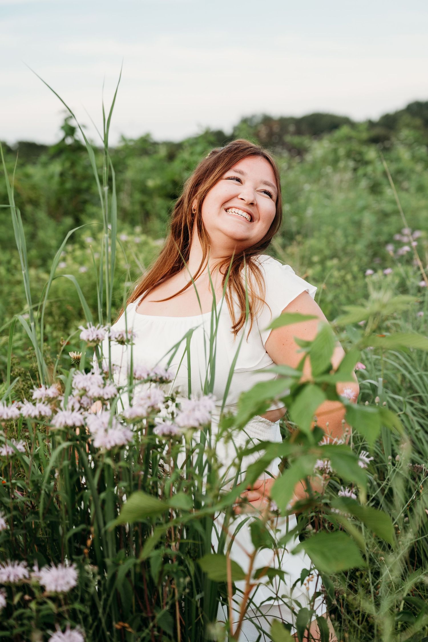 A joyful person sits in a meadow of wildflowers and tall grass on a bright summer day.