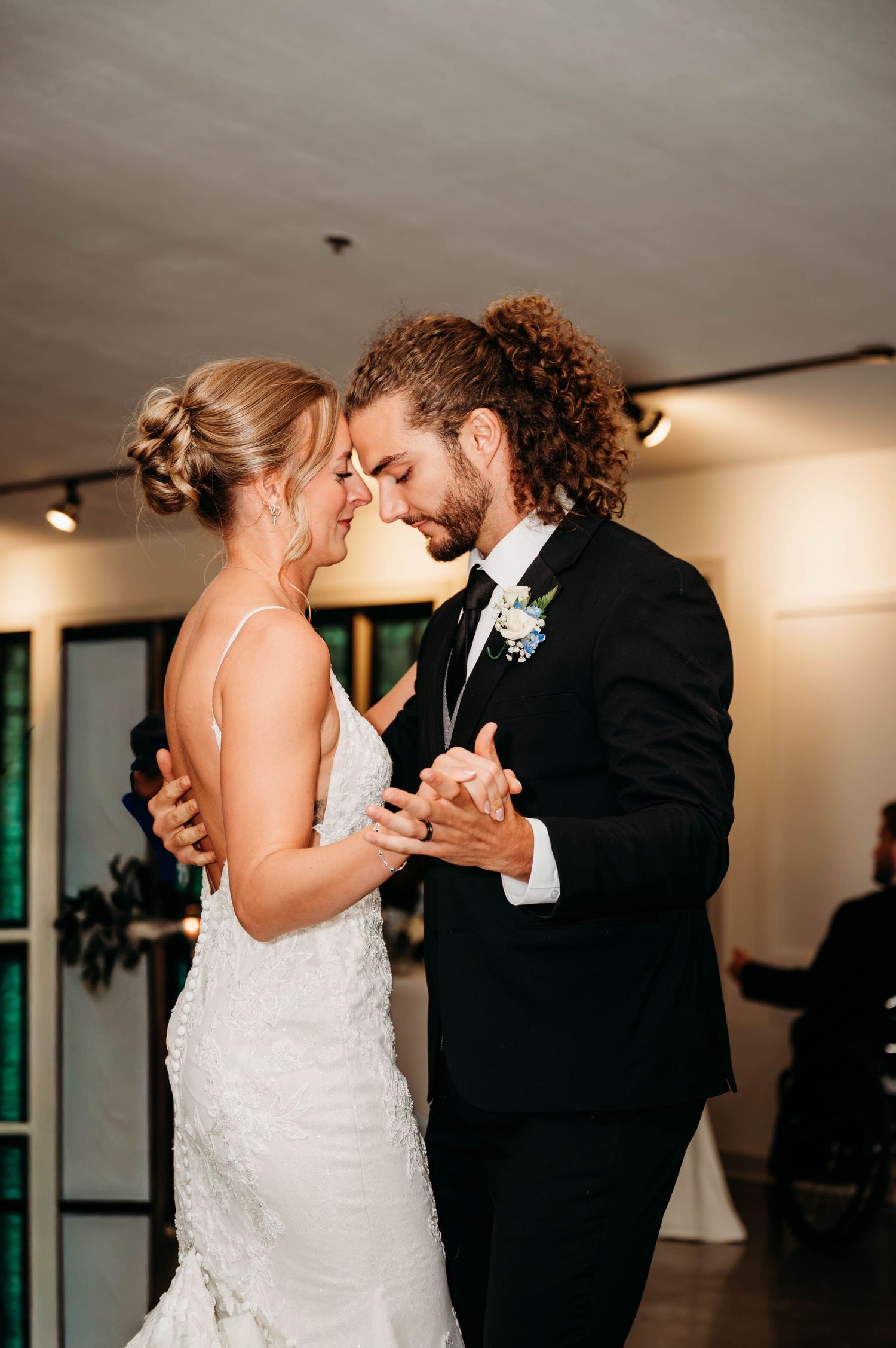 Bride and groom share an intimate first dance, touching foreheads, dressed in wedding attire at their reception.