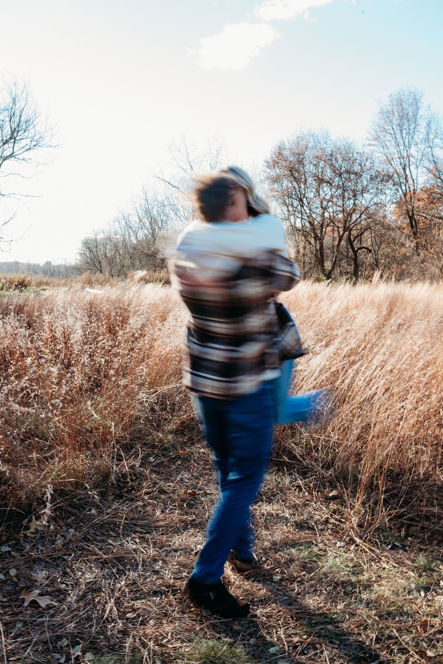 Motion blur captures a couple dancing together in a golden autumn field with dried grass and bare trees.