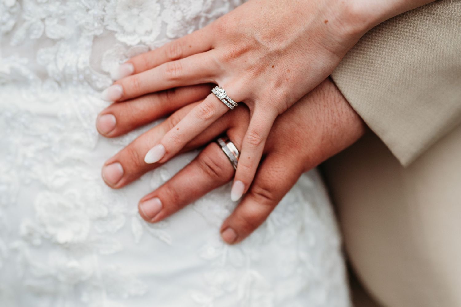 Close-up view of hands wearing engagement rings against a white textured background.