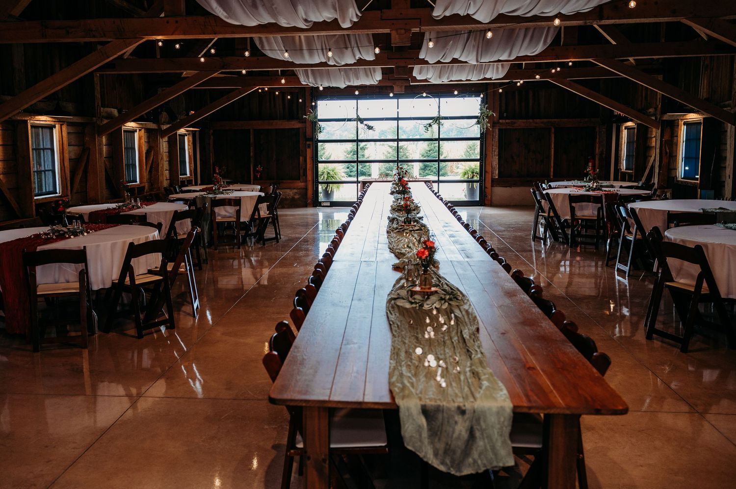 Rustic barn wedding reception with long wooden farm tables, string lights, and elegant white draping.
