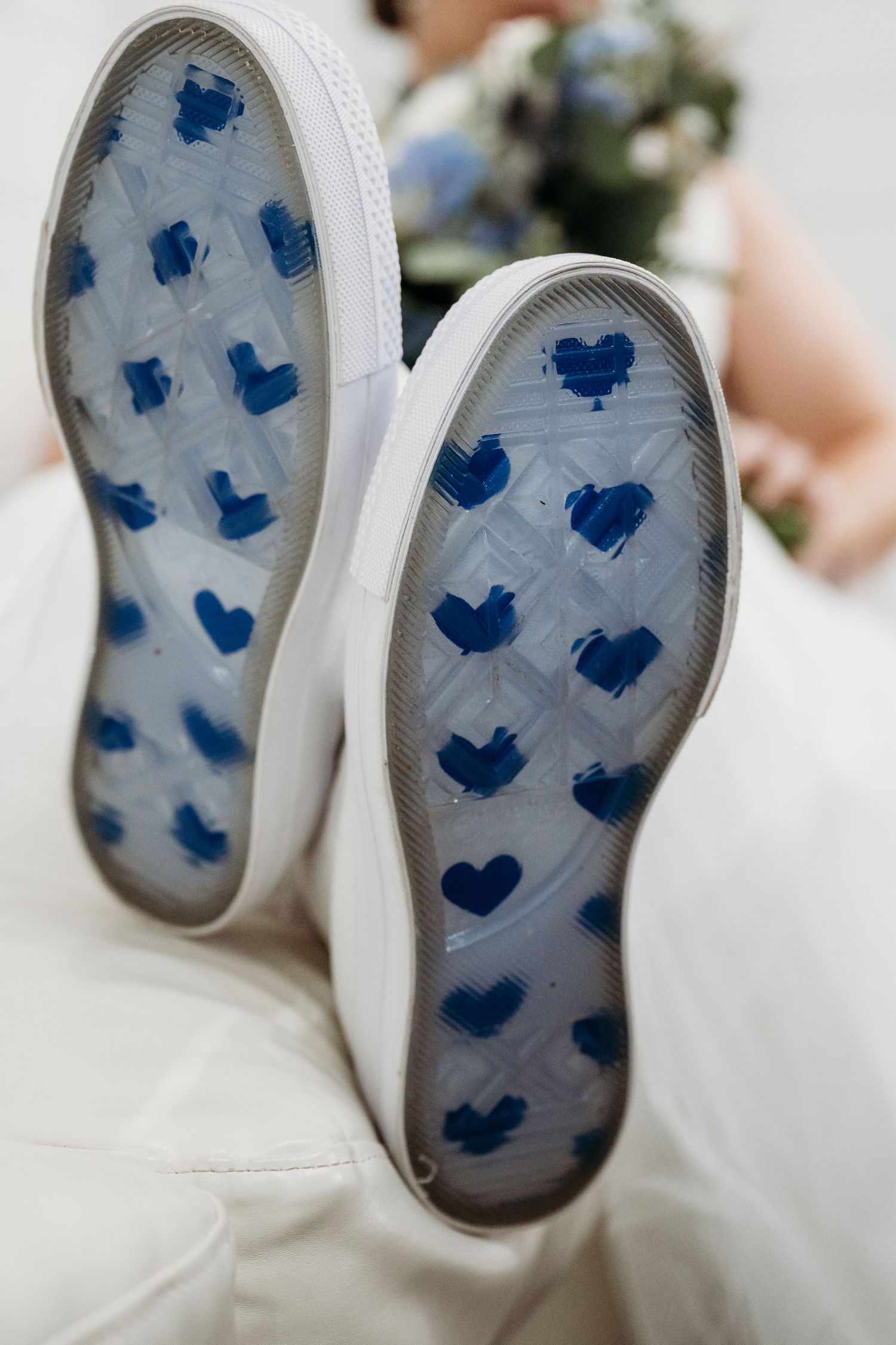 White baby shoes with blue heart patterns on the soles shown from different angles on a light background.