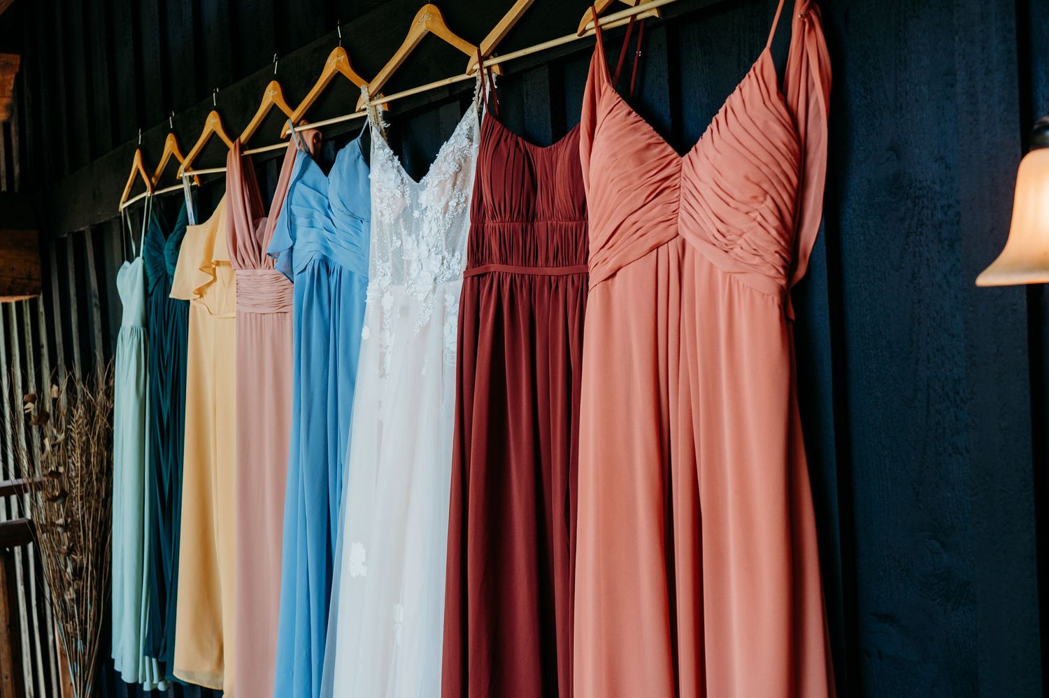 A row of colorful bridesmaid dresses hanging on display with shades of pink, blue, and yellow in a boutique setting.