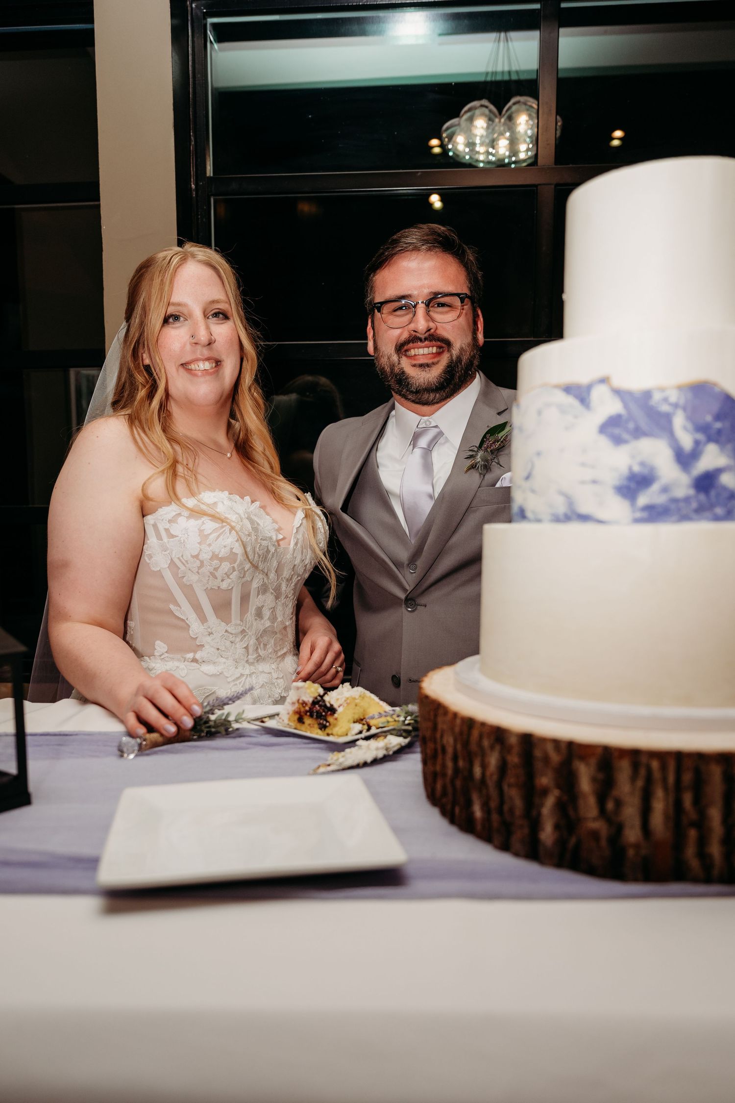Wedding couple enjoys cake and desserts at their reception table with rustic wood decor and elegant white details.