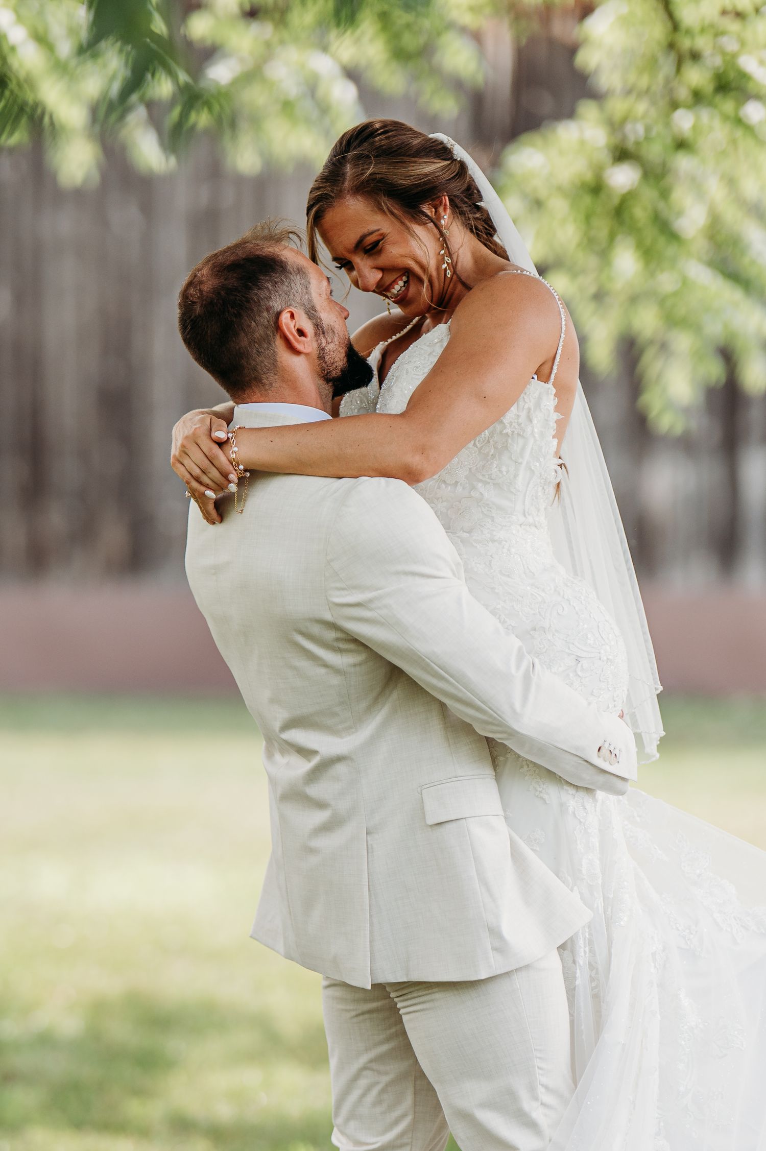 A romantic wedding couple embraces outdoors in a garden setting with soft natural lighting.