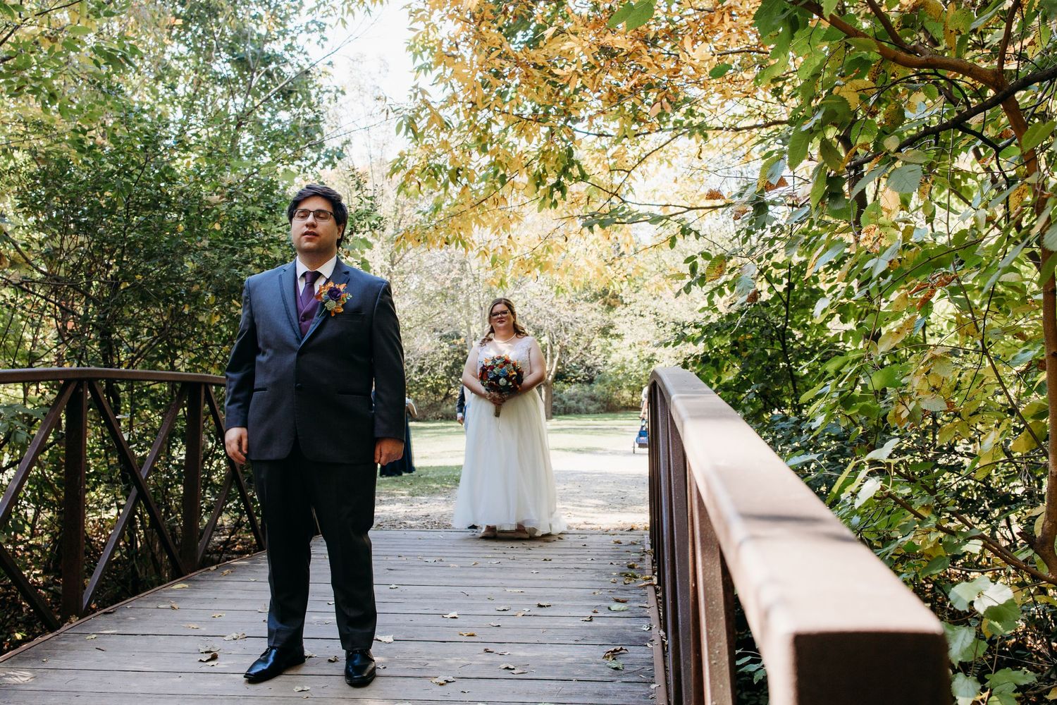 Couple standing on a wooden bridge during fall wedding ceremony with autumn foliage in background.
