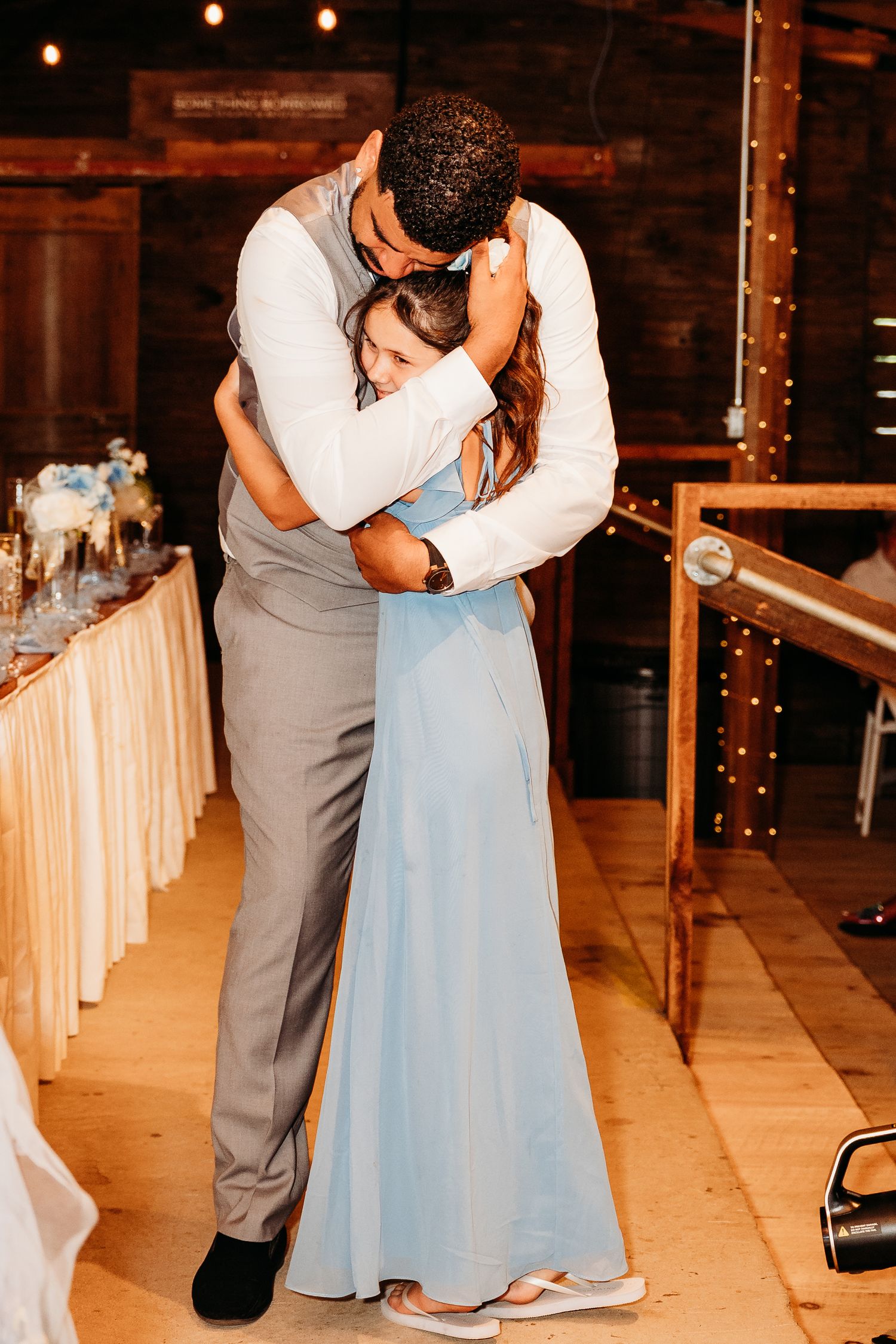A romantic slow dance moment captured on a warmly lit dance floor with string lights.