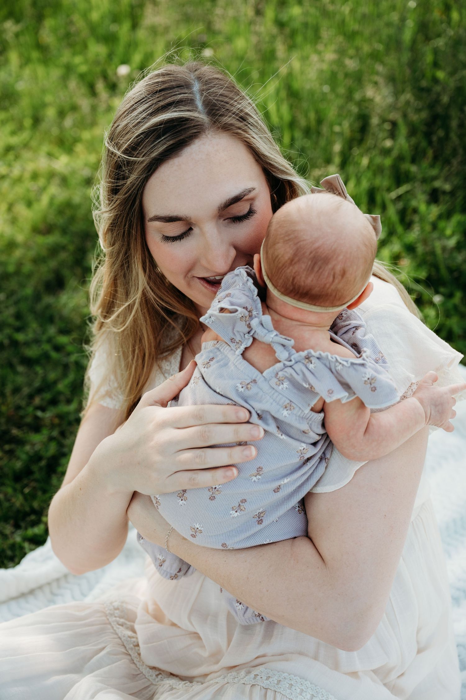 A tender moment between parent and baby outdoors in a garden setting with lush green foliage in the background.